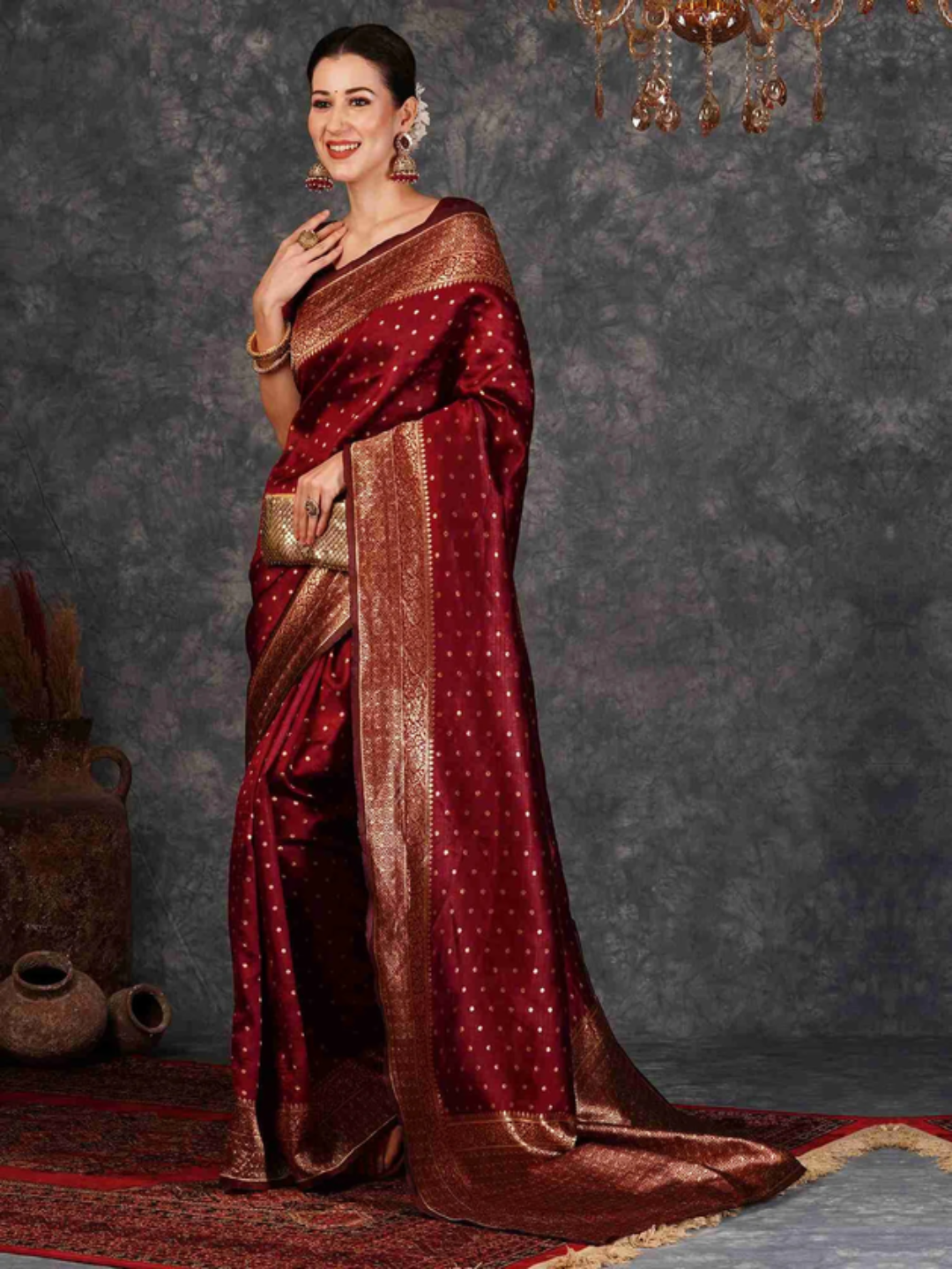 Woman wearing a red saree with gold patterns against a dark textured wall.