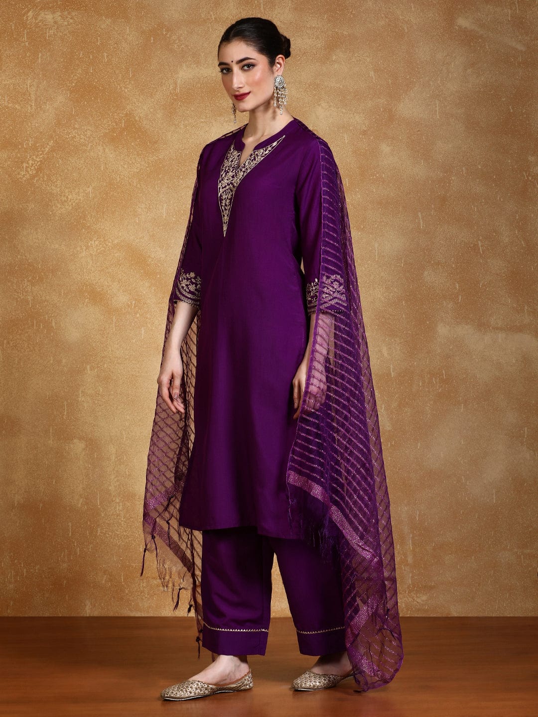 Woman wearing a purple traditional outfit with gold embroidery against a brown background