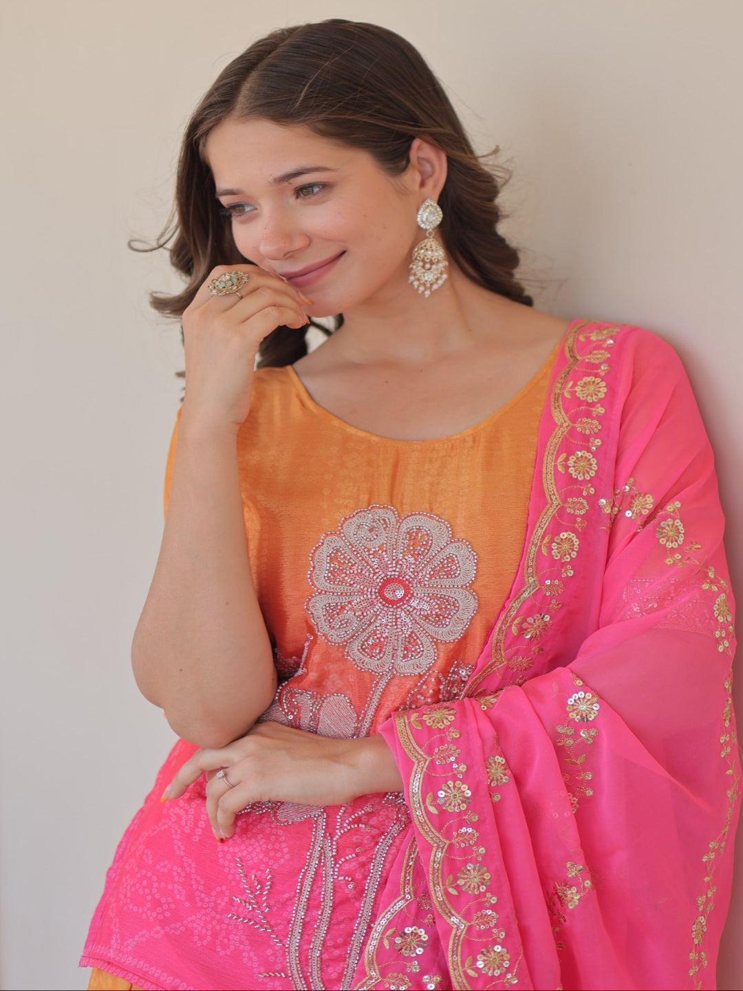 Woman wearing a pink and orange traditional outfit with floral patterns against a plain background