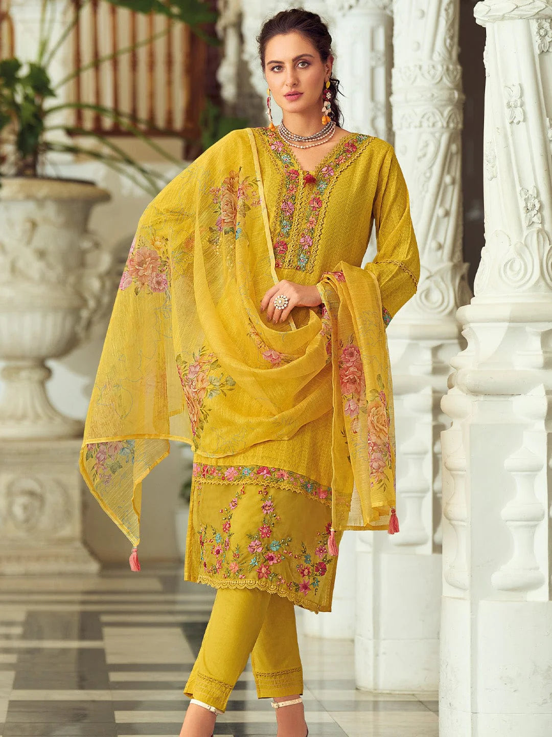 Woman wearing a yellow embroidered traditional outfit in an elegant indoor setting.