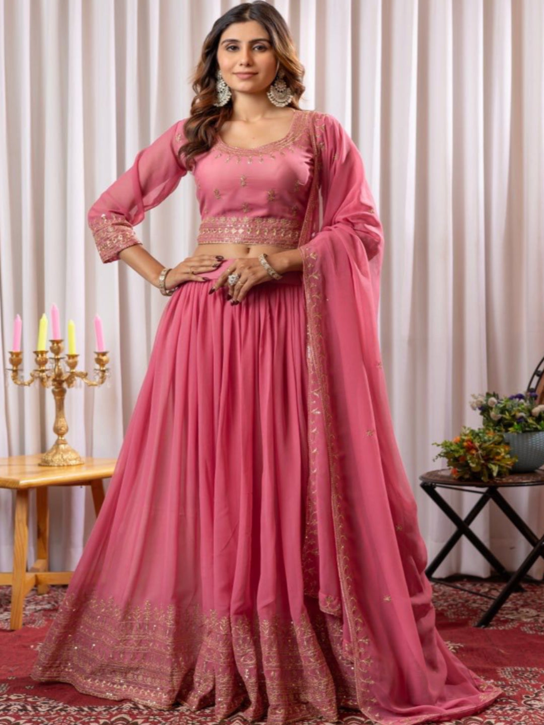 Woman in a pink traditional outfit standing in a decorated room with curtains and decorative items.