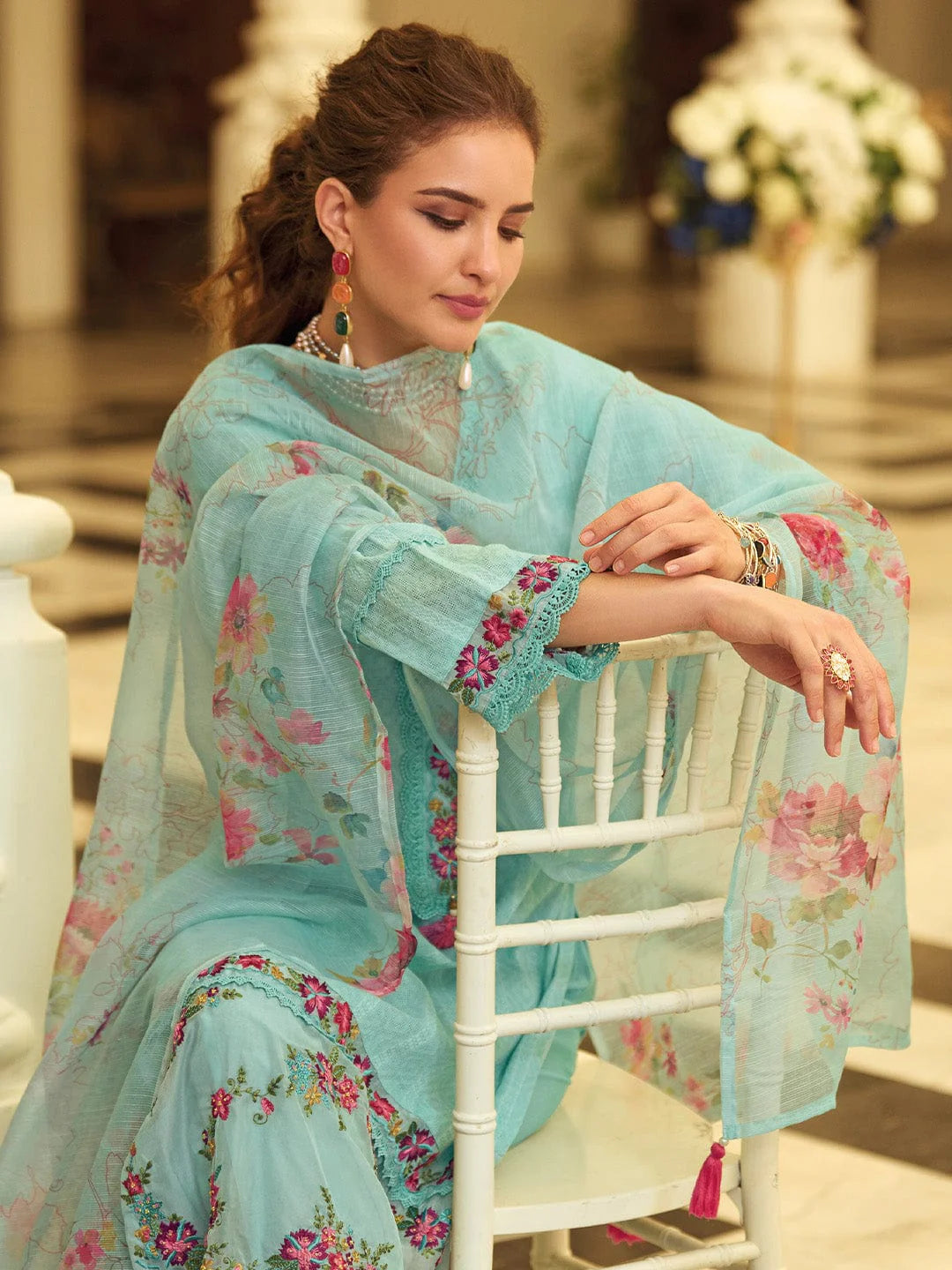 Woman in a light blue floral dress sitting on a white chair.