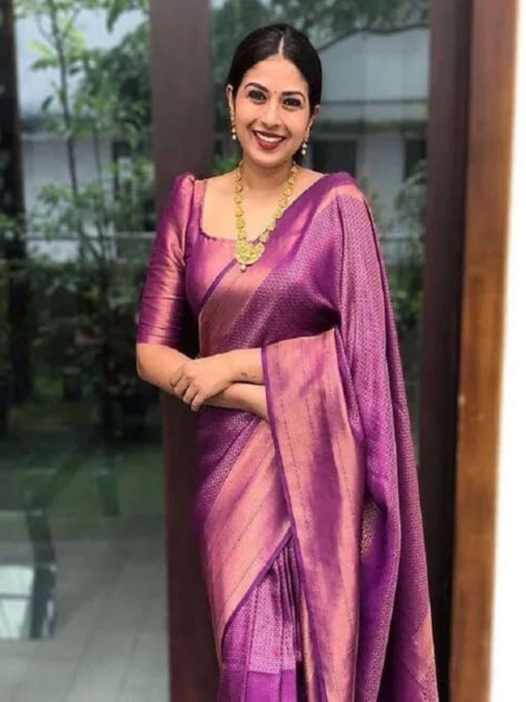 Woman wearing a purple saree with a matching blouse, standing outdoors.