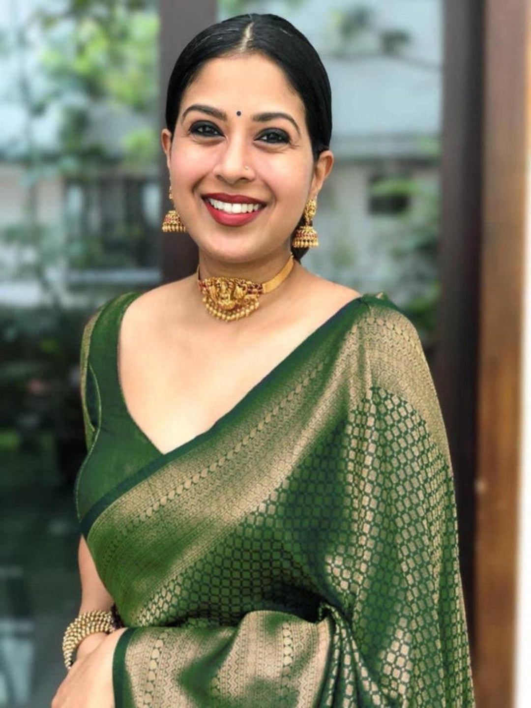 Woman wearing a green saree with gold jewelry indoors