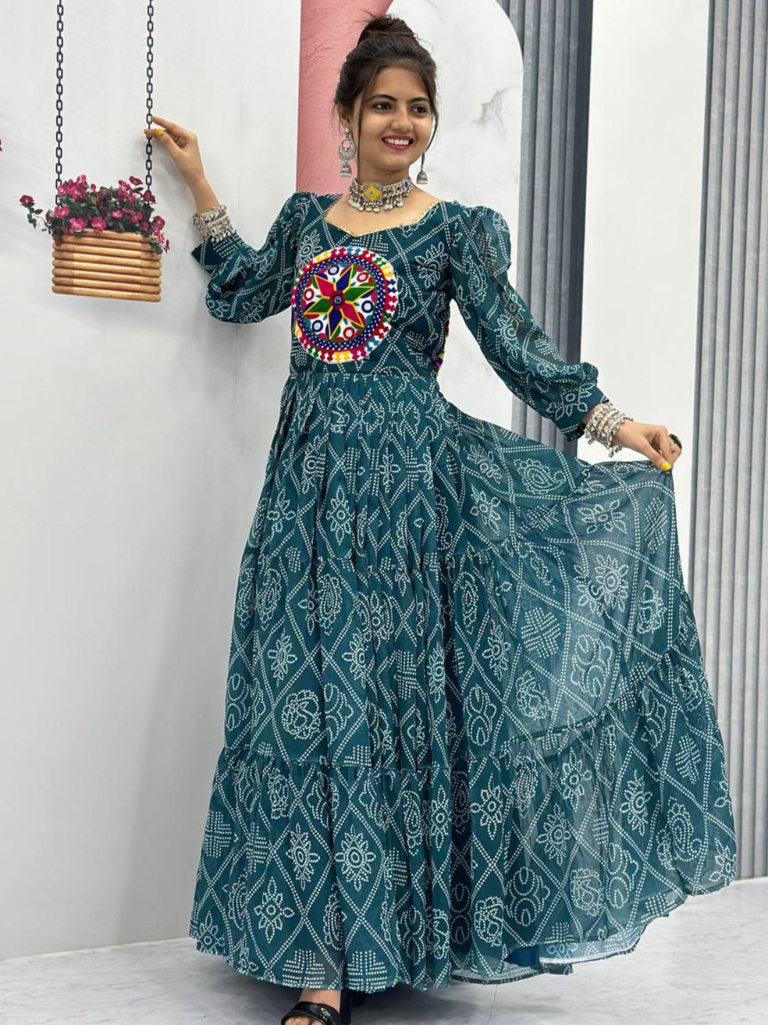 Woman wearing a teal patterned dress with a colorful circular design, standing indoors.