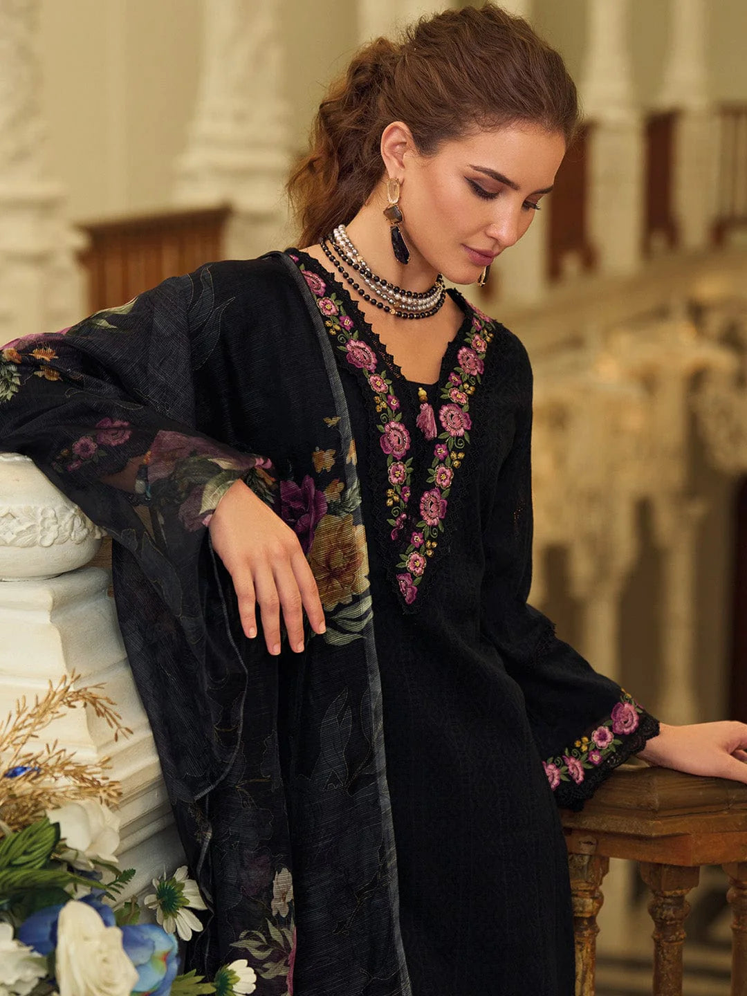 Woman wearing a black embroidered dress sitting on a decorative chair.