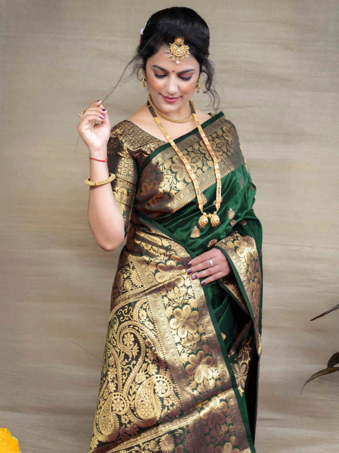 Woman wearing a traditional green and gold saree with jewelry against a neutral background