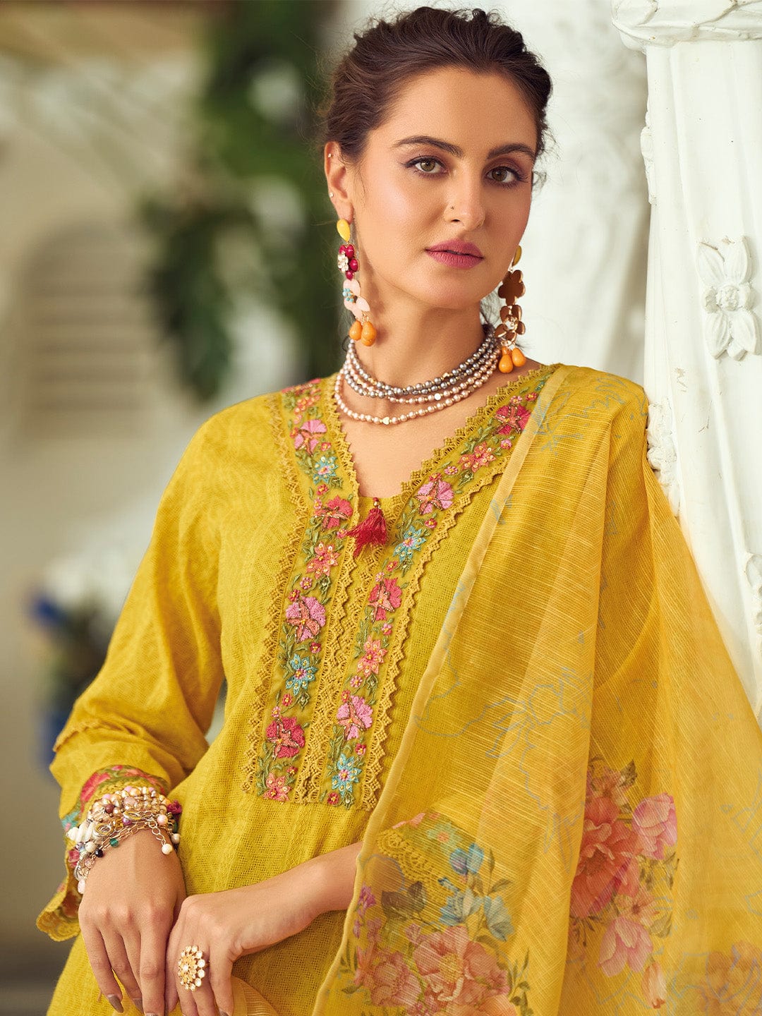 Woman wearing a yellow embroidered traditional outfit with jewelry indoors.