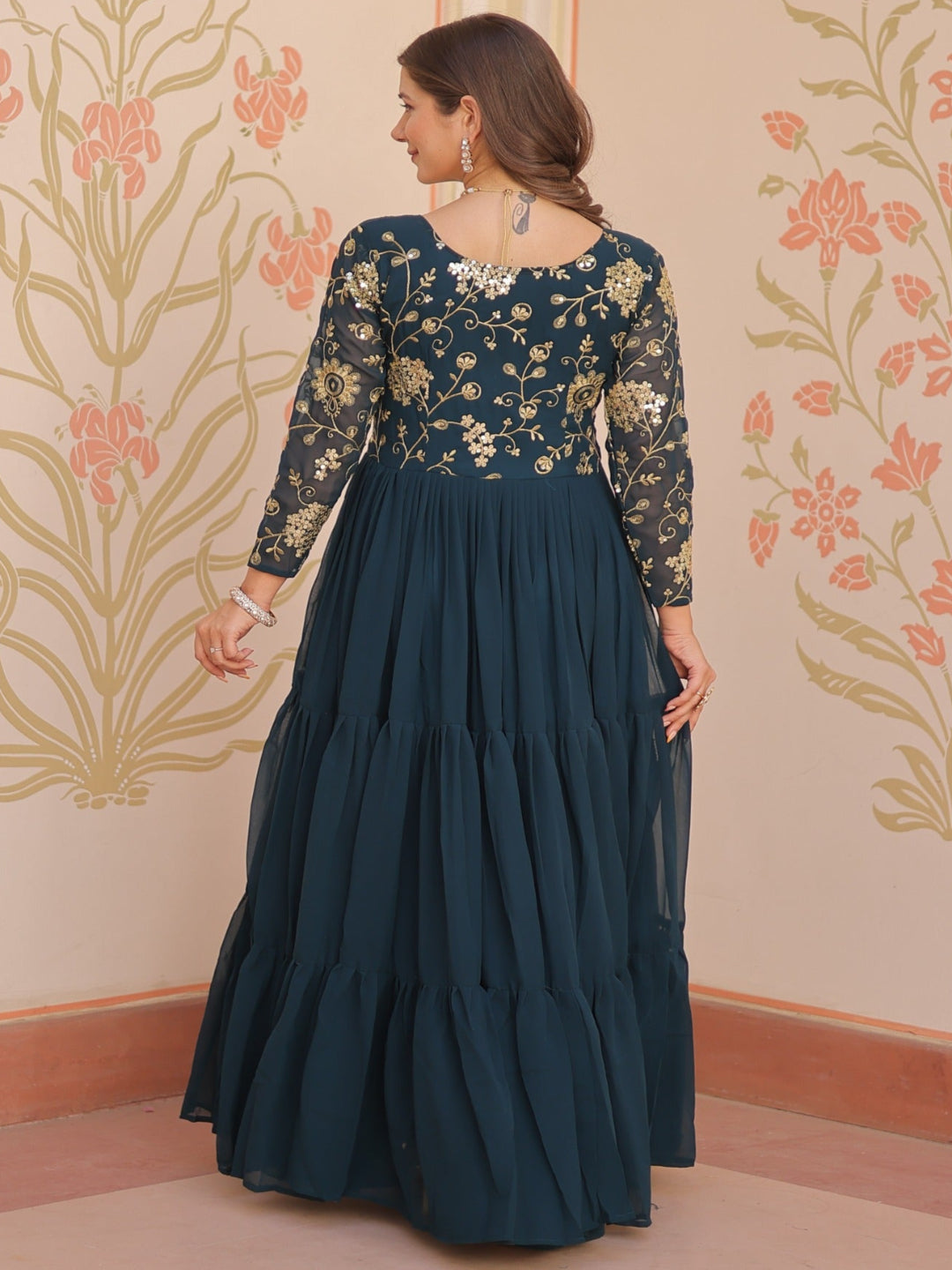 Woman wearing a dark blue traditional outfit with floral patterns in a decorated room.