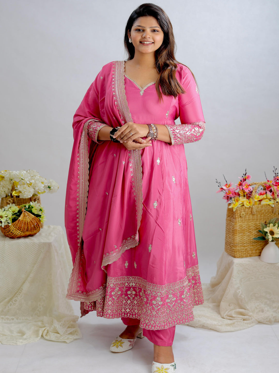 Woman in a pink traditional outfit standing between two floral arrangements on a white background