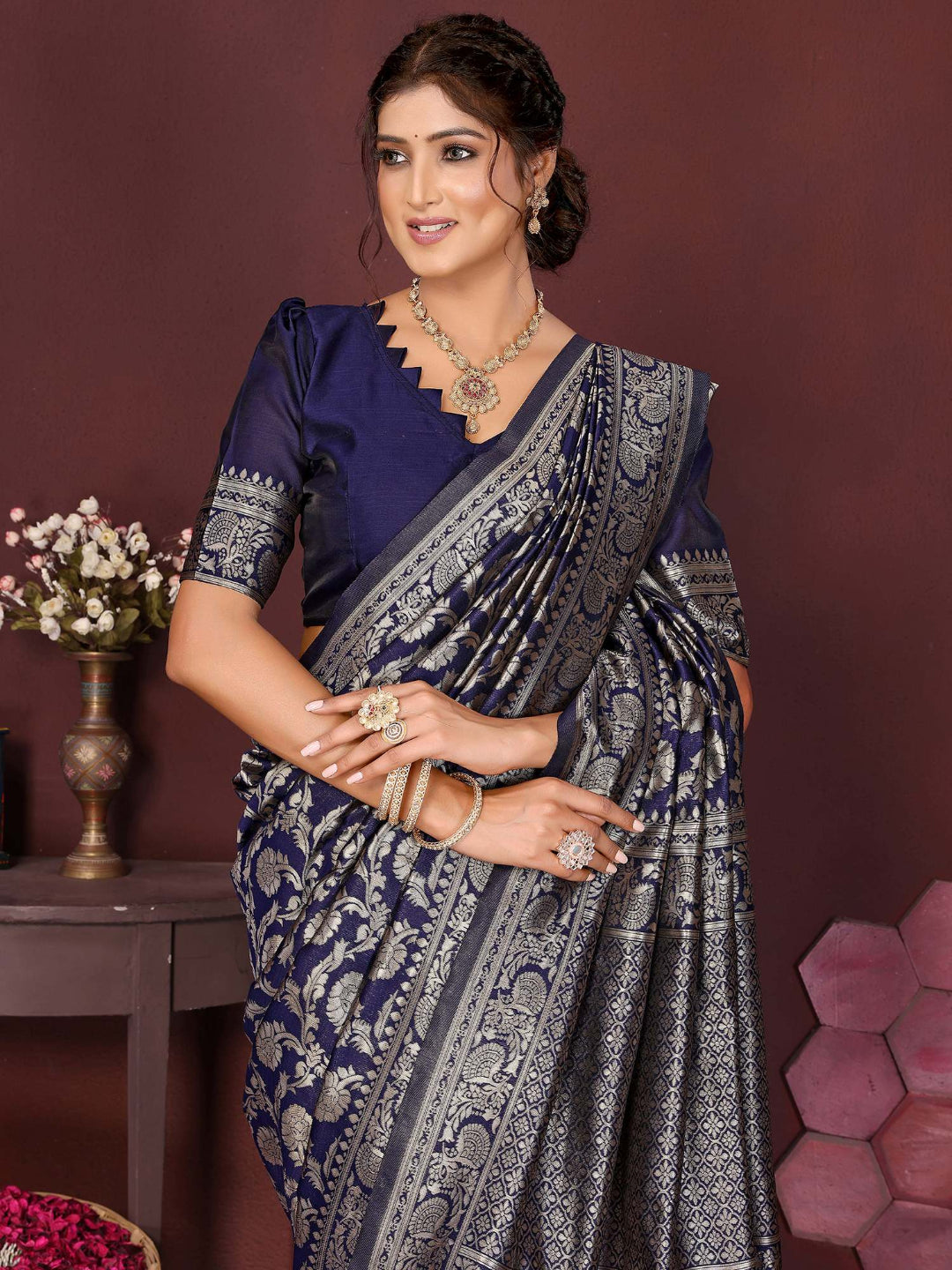 Woman wearing a traditional saree with a dark blue blouse and silver border against a purple background.