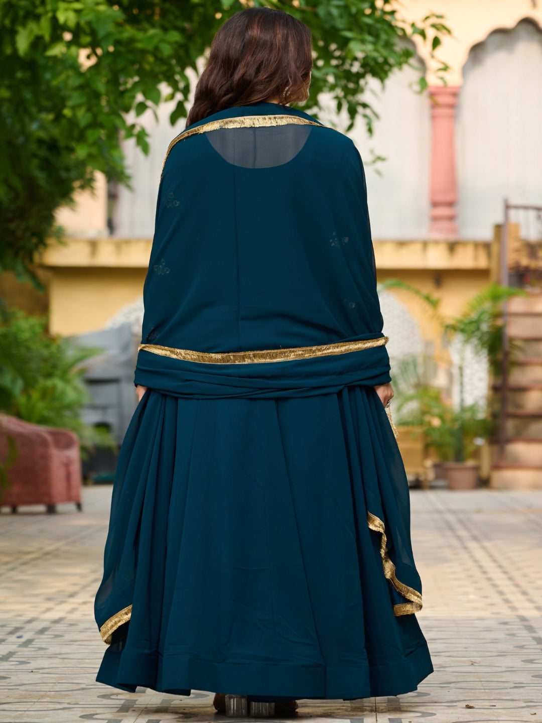 Person wearing a teal dress with gold accents in an outdoor setting