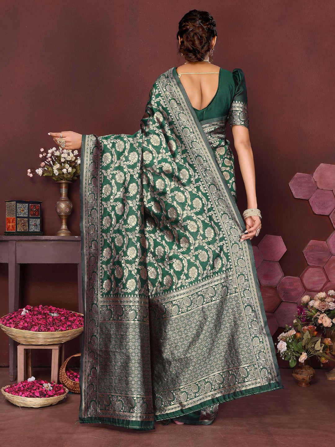 Woman wearing a green saree with a pattern, standing against a brown background with decorative elements.