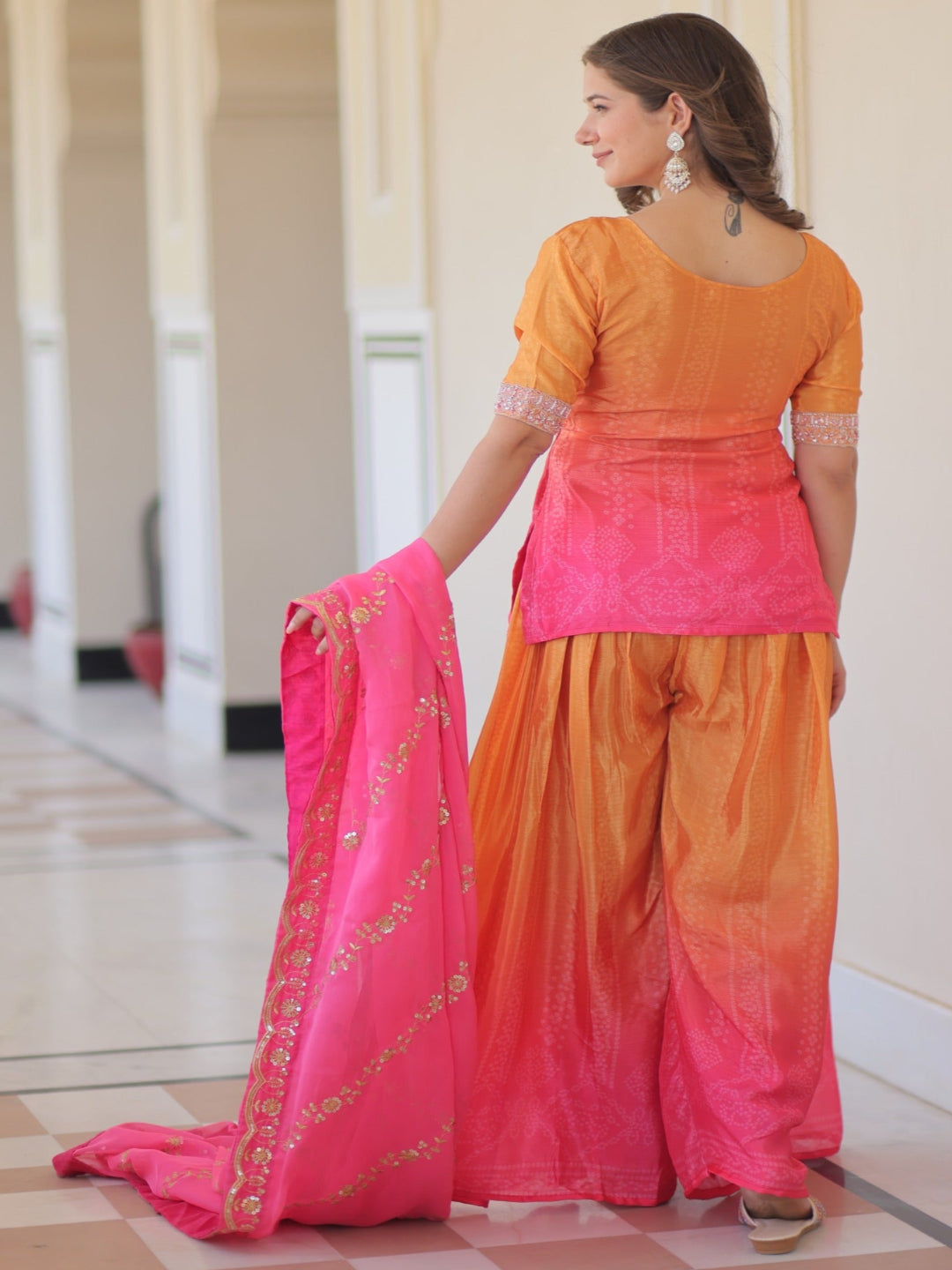 Woman in a traditional outfit with pink and orange colors standing in a hallway.