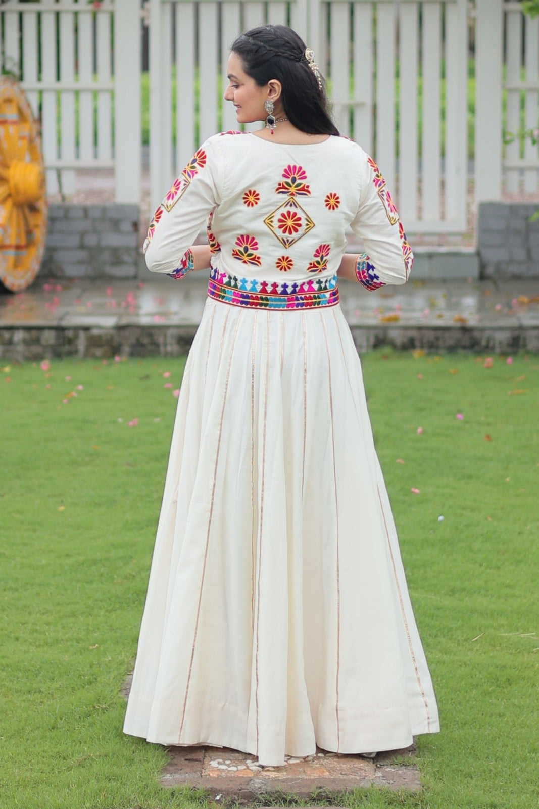 Woman in a traditional outfit standing in a garden with floral decorations.