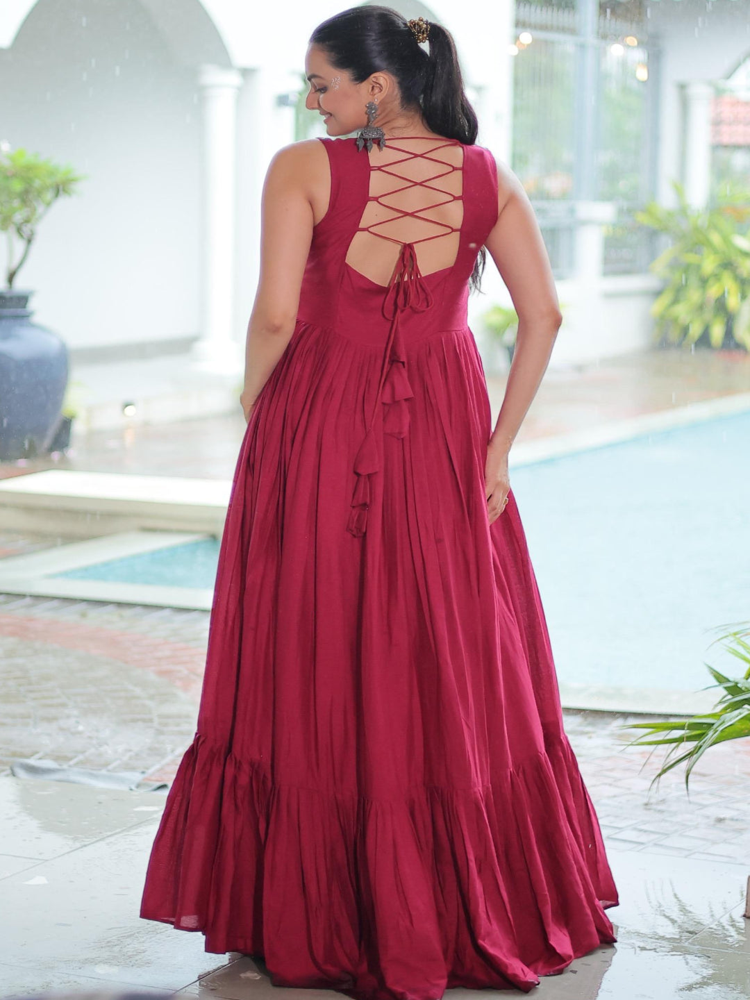 Woman wearing a red dress with an open back, standing by a poolside.