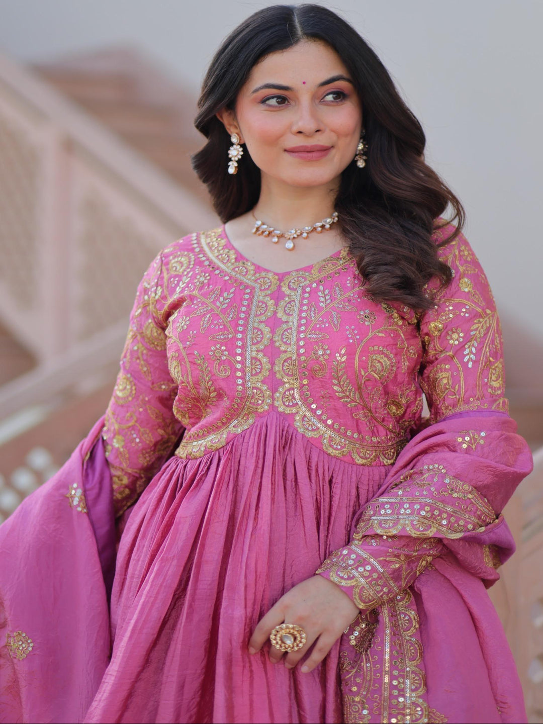 Woman in a pink traditional outfit with gold embroidery indoors.