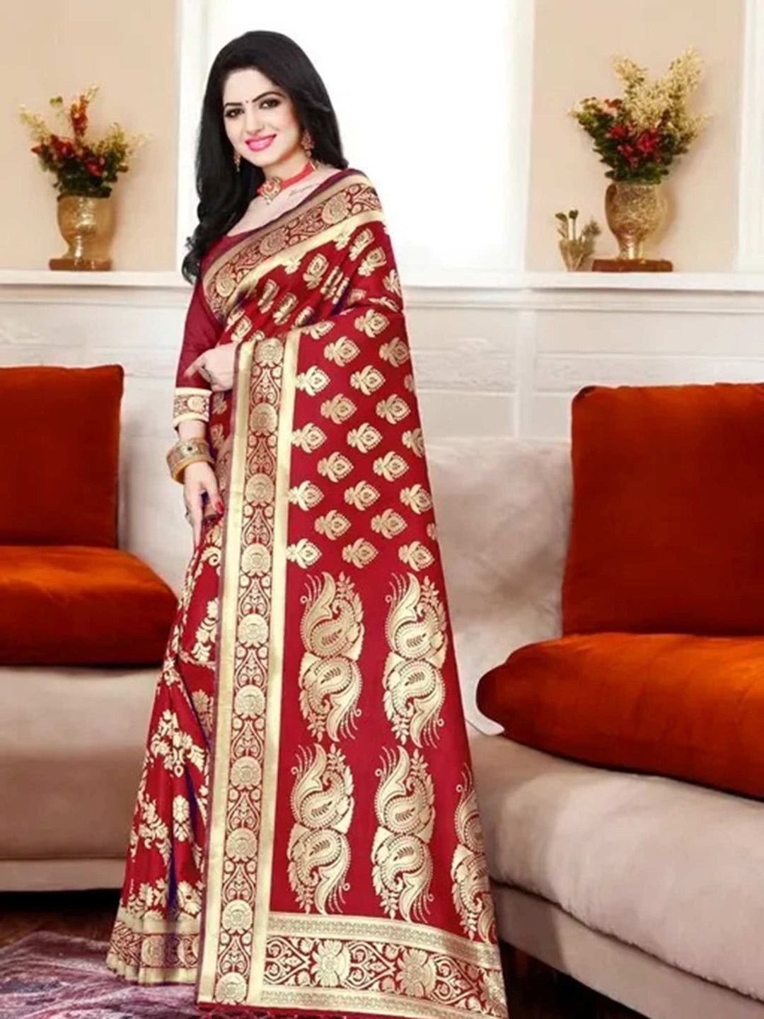 Woman wearing a red saree with gold patterns in a living room setting.
