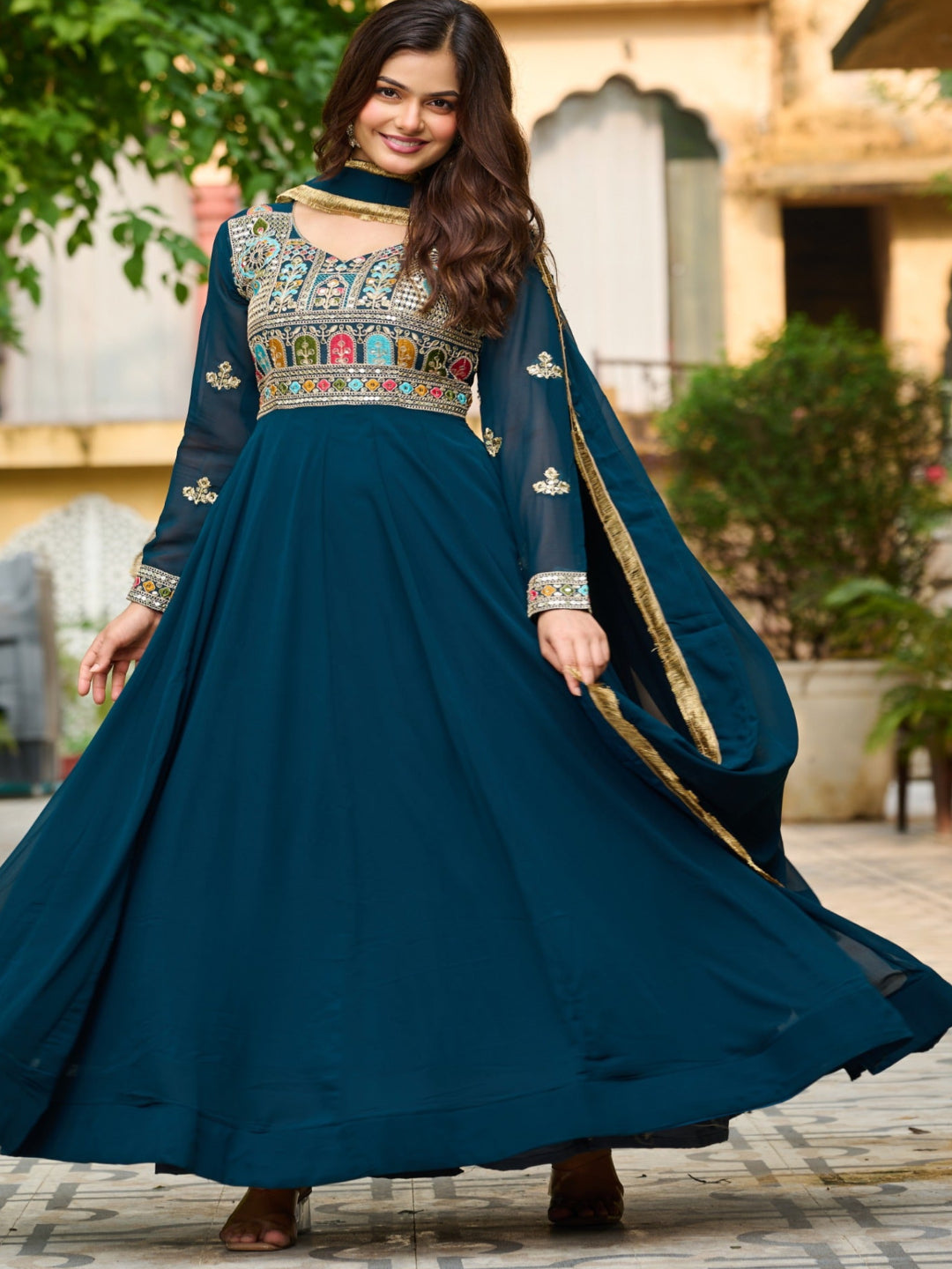 Woman in a blue traditional outfit with intricate designs standing outdoors.