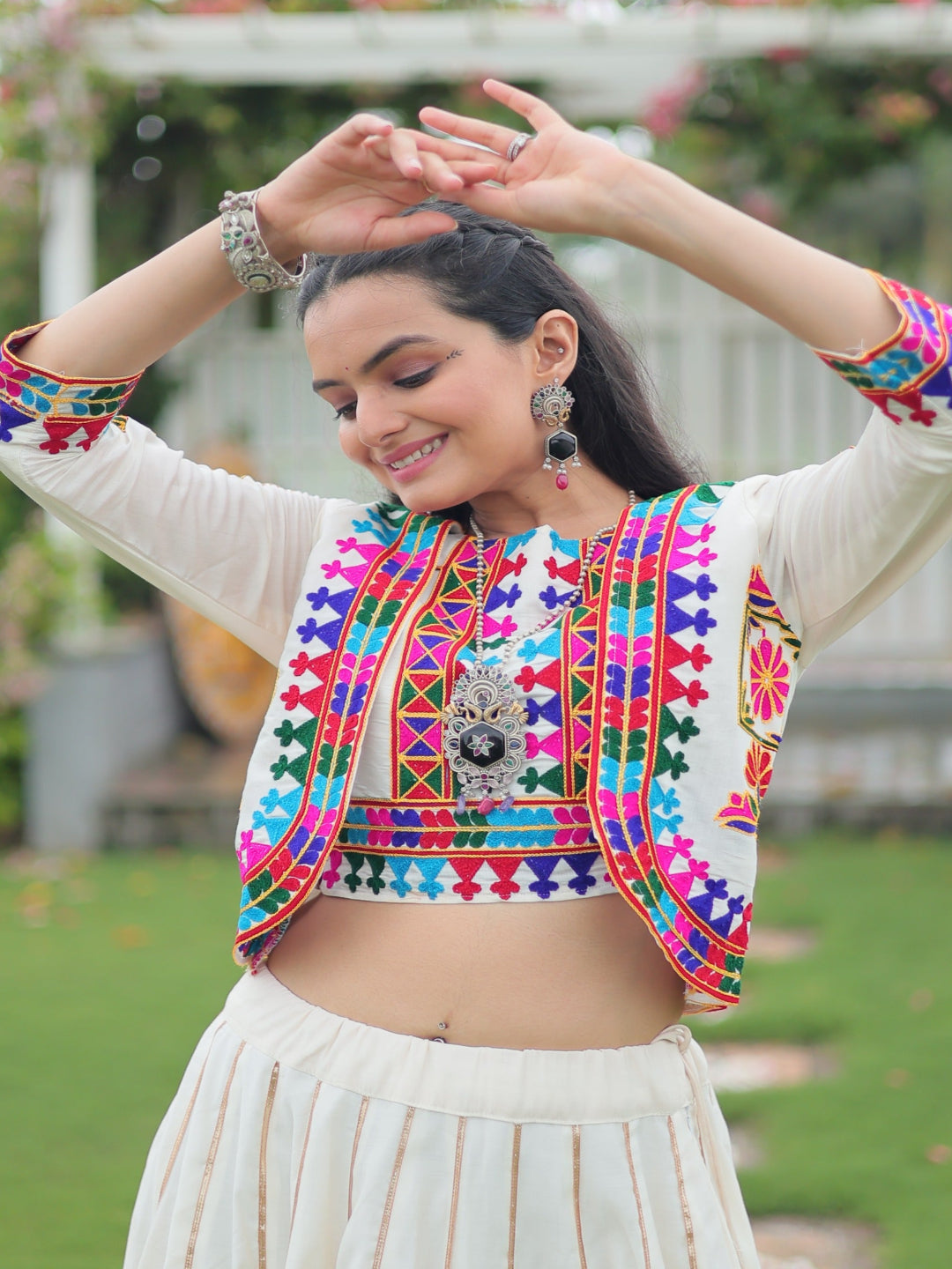 Woman in traditional multicolored blouse with intricate patterns and white skirt outdoors.