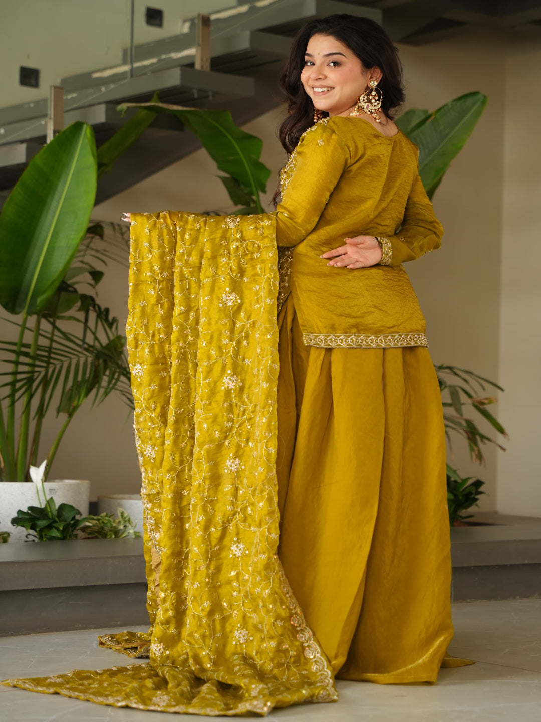 Woman in a mustard yellow traditional outfit holding a matching dupatta in an indoor setting.