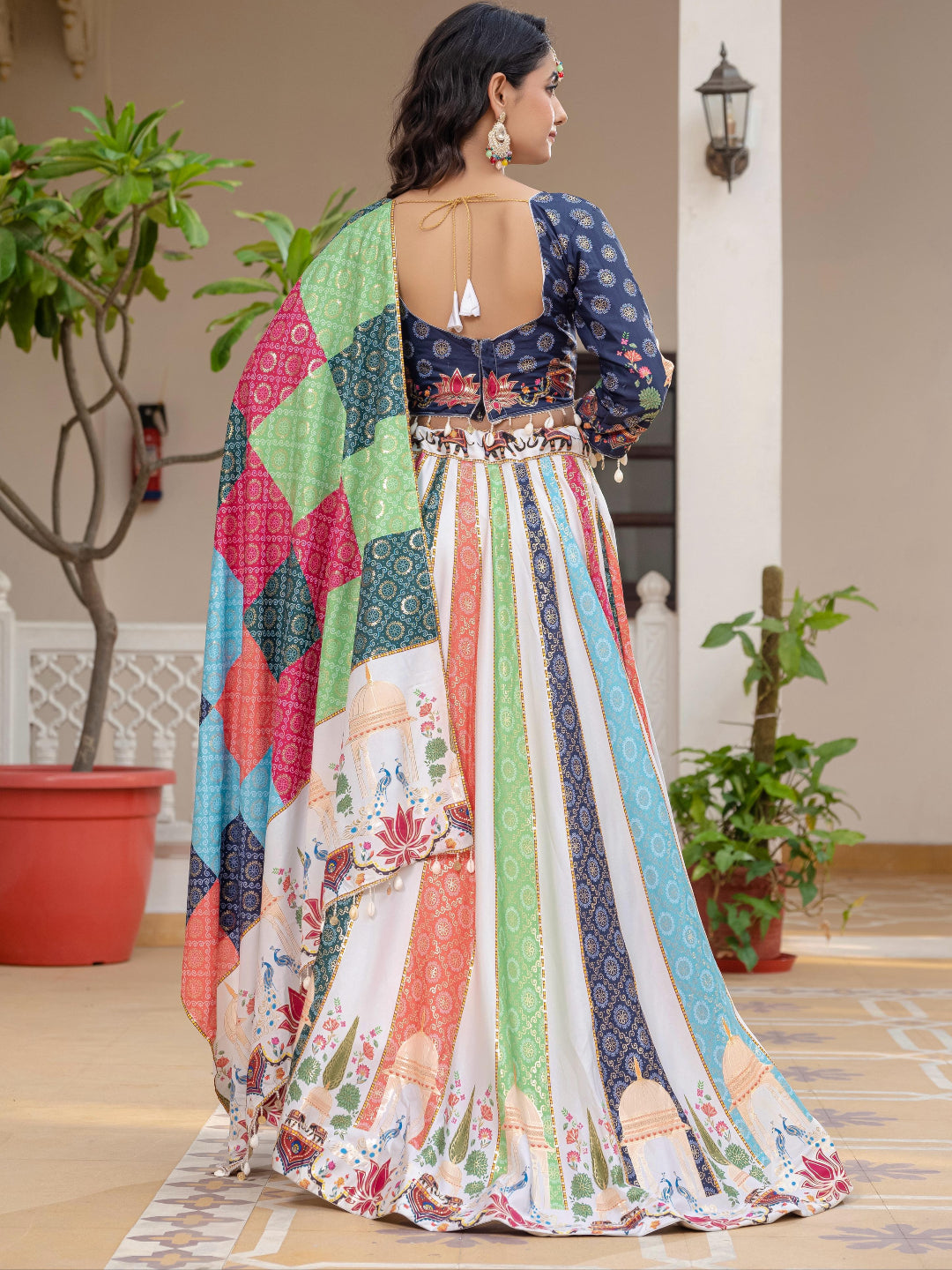 Woman wearing a colorful patterned dress in an indoor setting with plants and a lamp.