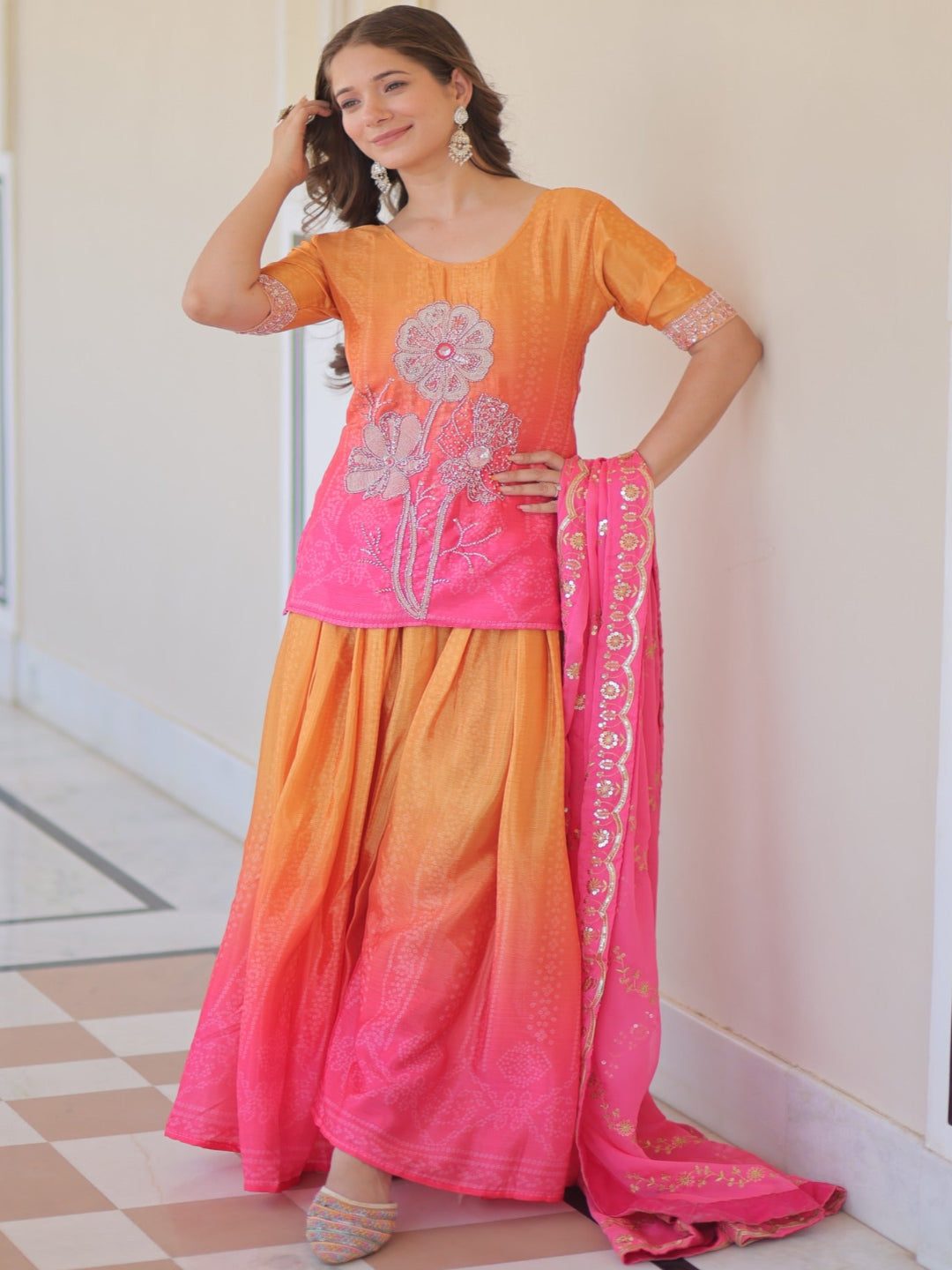 Woman wearing a pink and orange traditional outfit with floral patterns indoors.