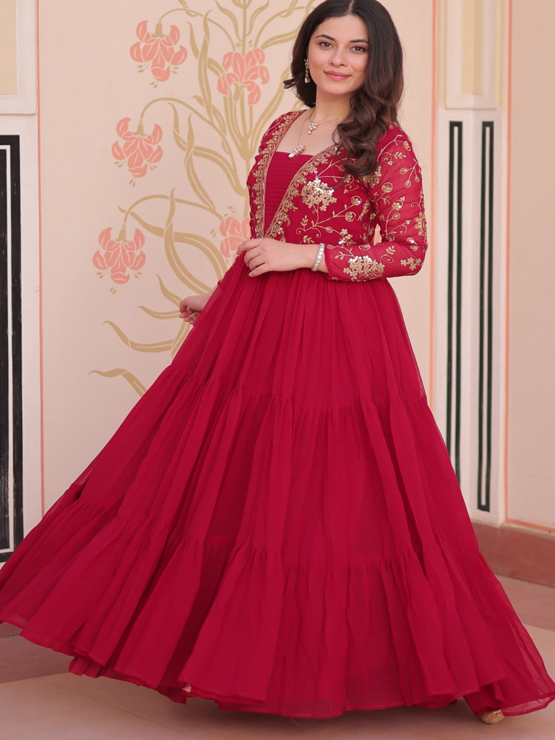 Woman in a red traditional outfit standing against a decorated wall.