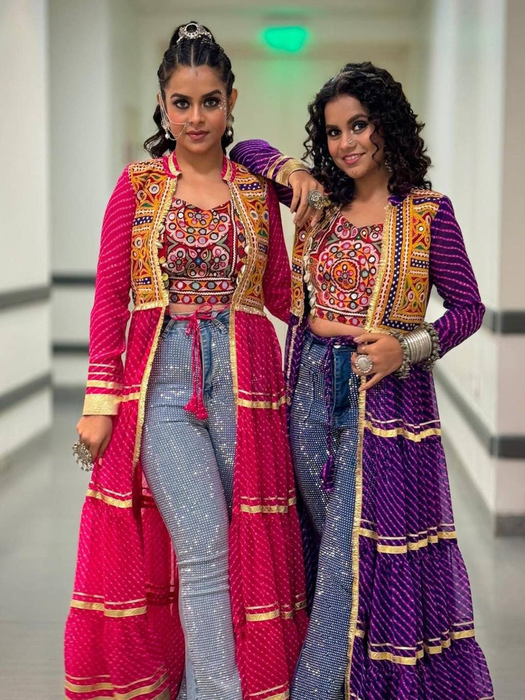 Two women in colorful traditional outfits posing together indoors.