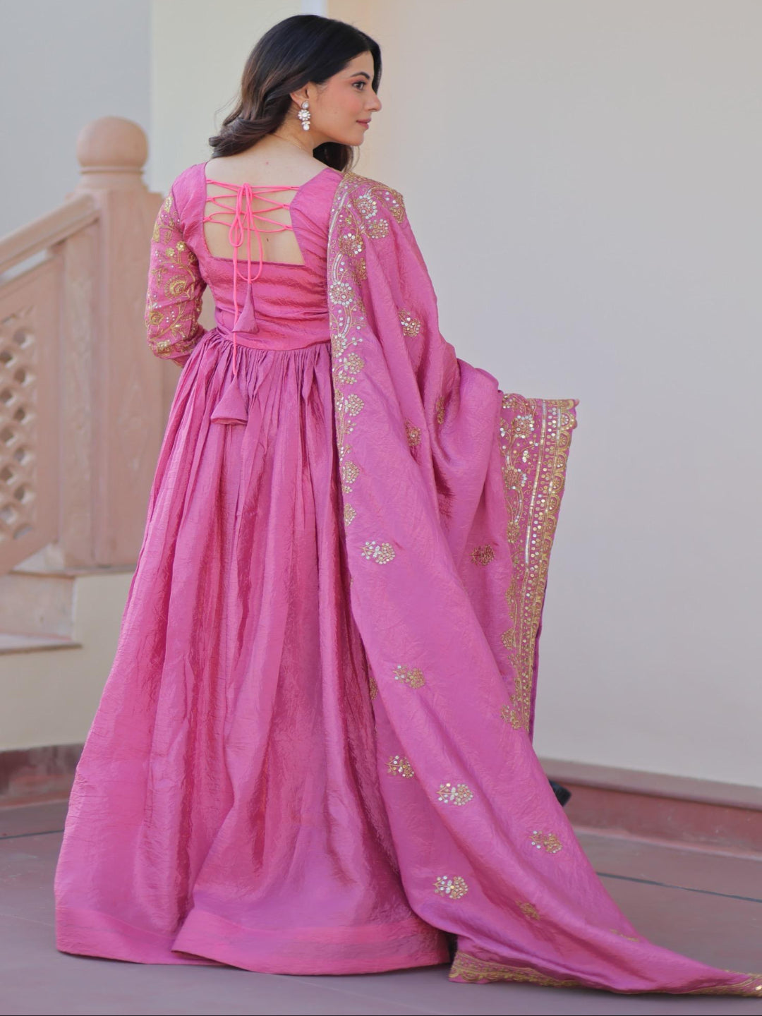 Woman in a pink traditional outfit with a matching dupatta, standing indoors.