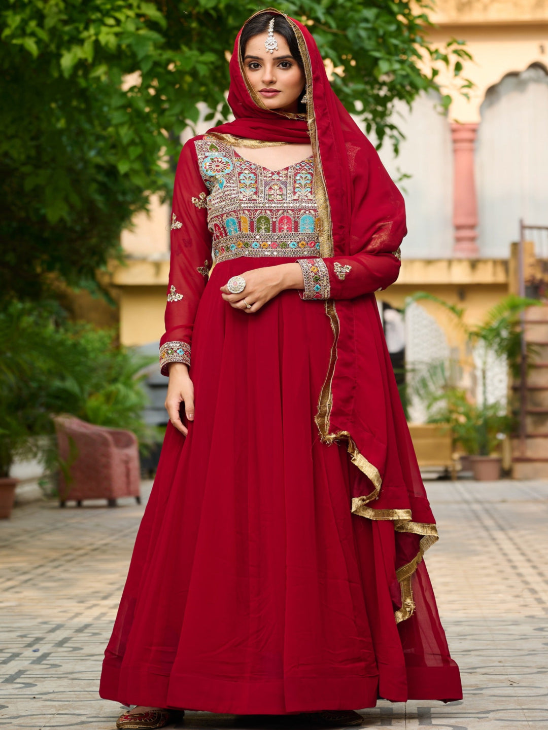 Woman in a red traditional outfit with intricate patterns standing outdoors.