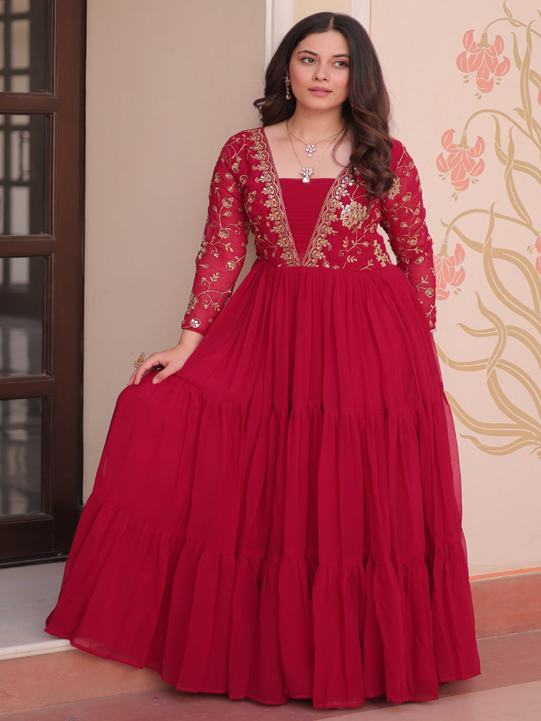 Woman wearing a red traditional outfit with intricate designs in a decorated room.