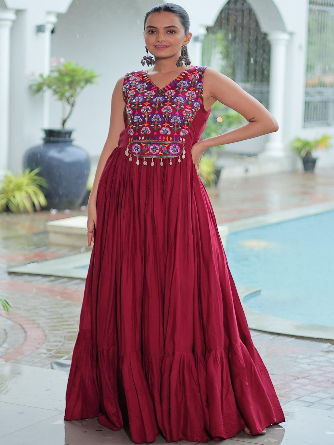 Woman in a long red dress with intricate patterns standing in an outdoor setting.