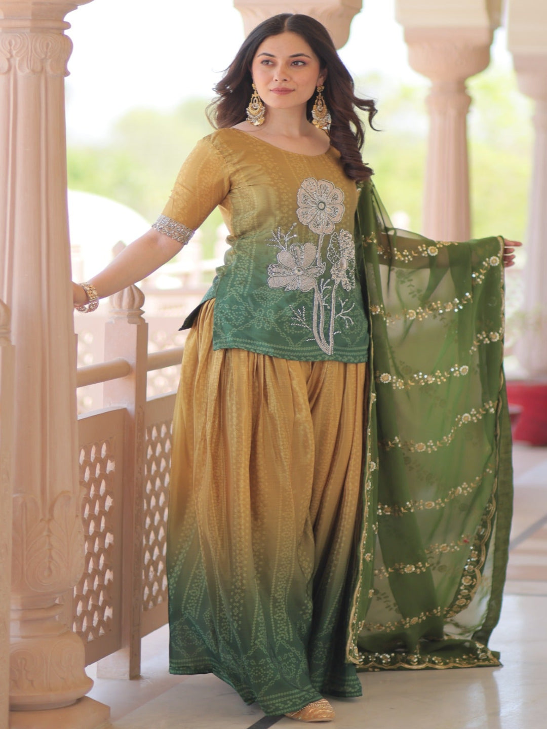 Woman in a green and yellow traditional outfit standing in a decorative architectural setting.
