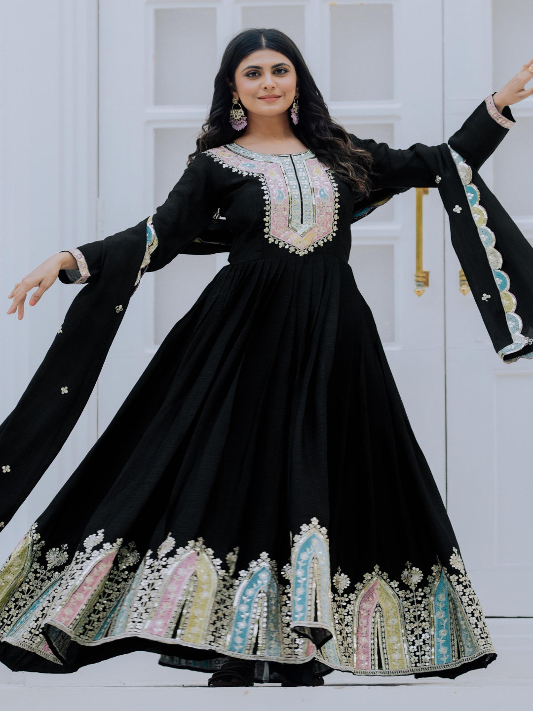 Woman wearing a black embroidered dress with long sleeves against a white door background