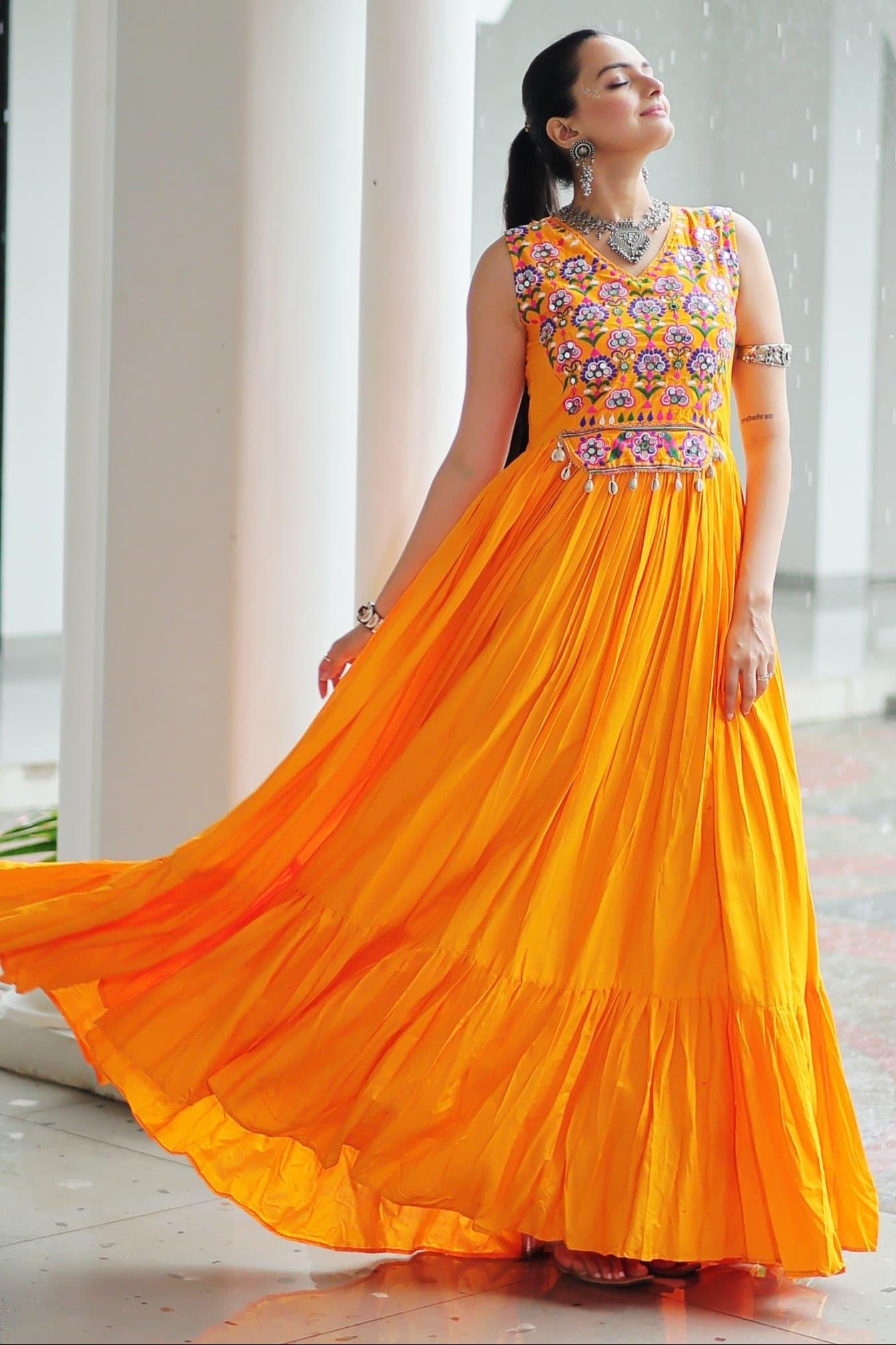 Woman in a bright orange traditional outfit with floral patterns indoors.