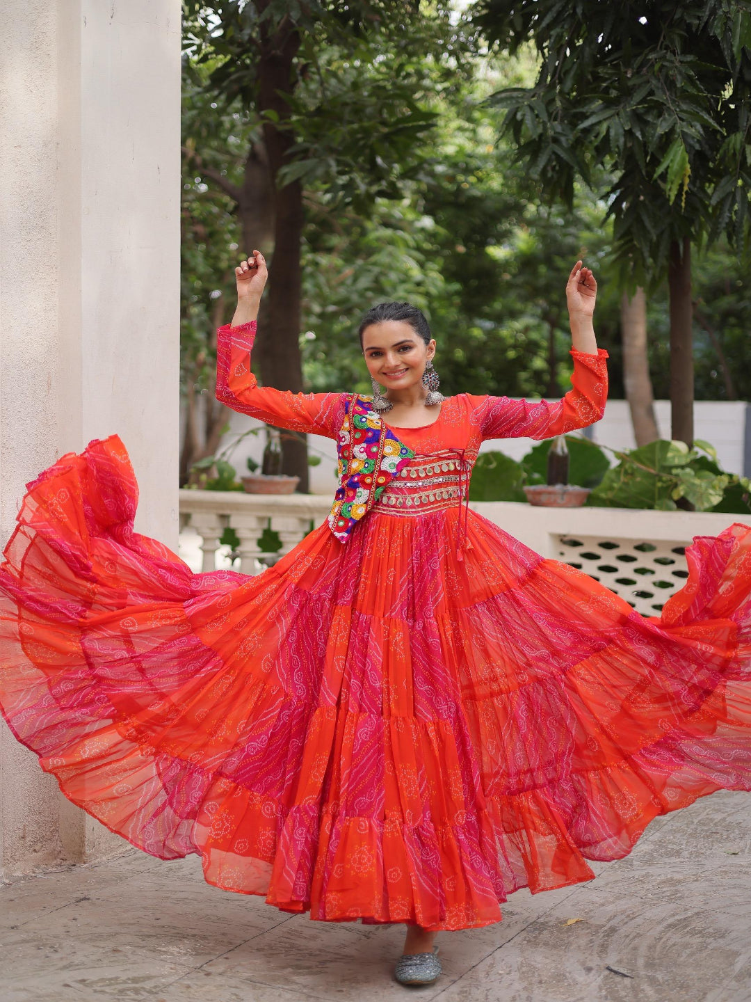 Woman in a vibrant red and pink traditional outfit with a colorful necklace, standing outdoors.