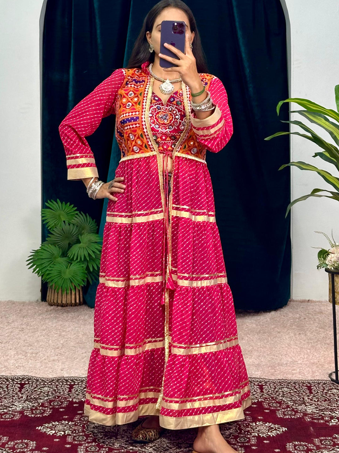 Person wearing a vibrant traditional outfit with a pink and orange patterned dress, standing in front of a mirror.