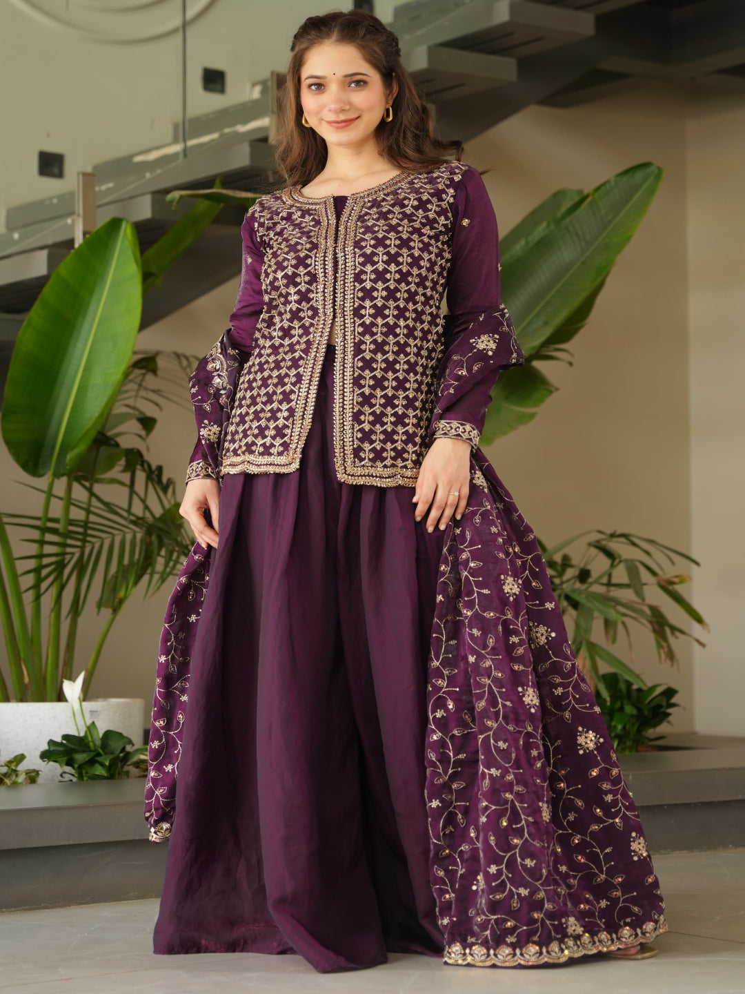 Woman wearing a purple embroidered outfit in an indoor setting with plants.