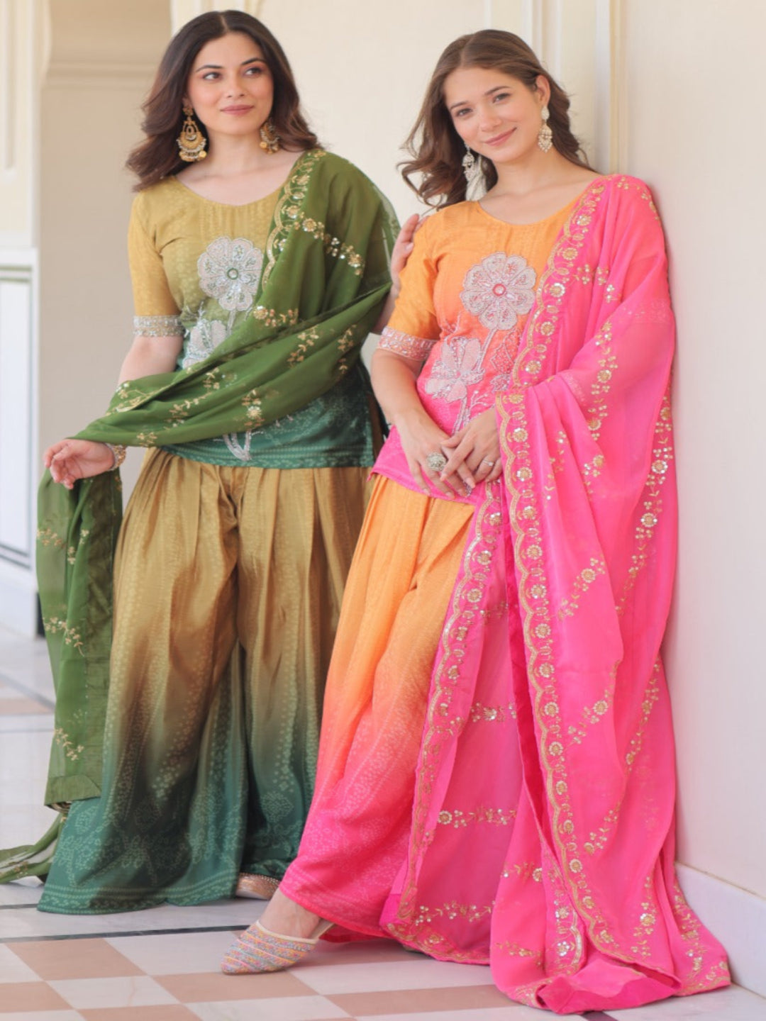Two women in traditional Indian attire standing against a decorative wall.