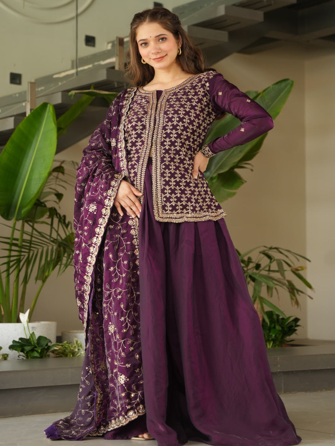 Woman in a traditional outfit standing indoors with plants in the background