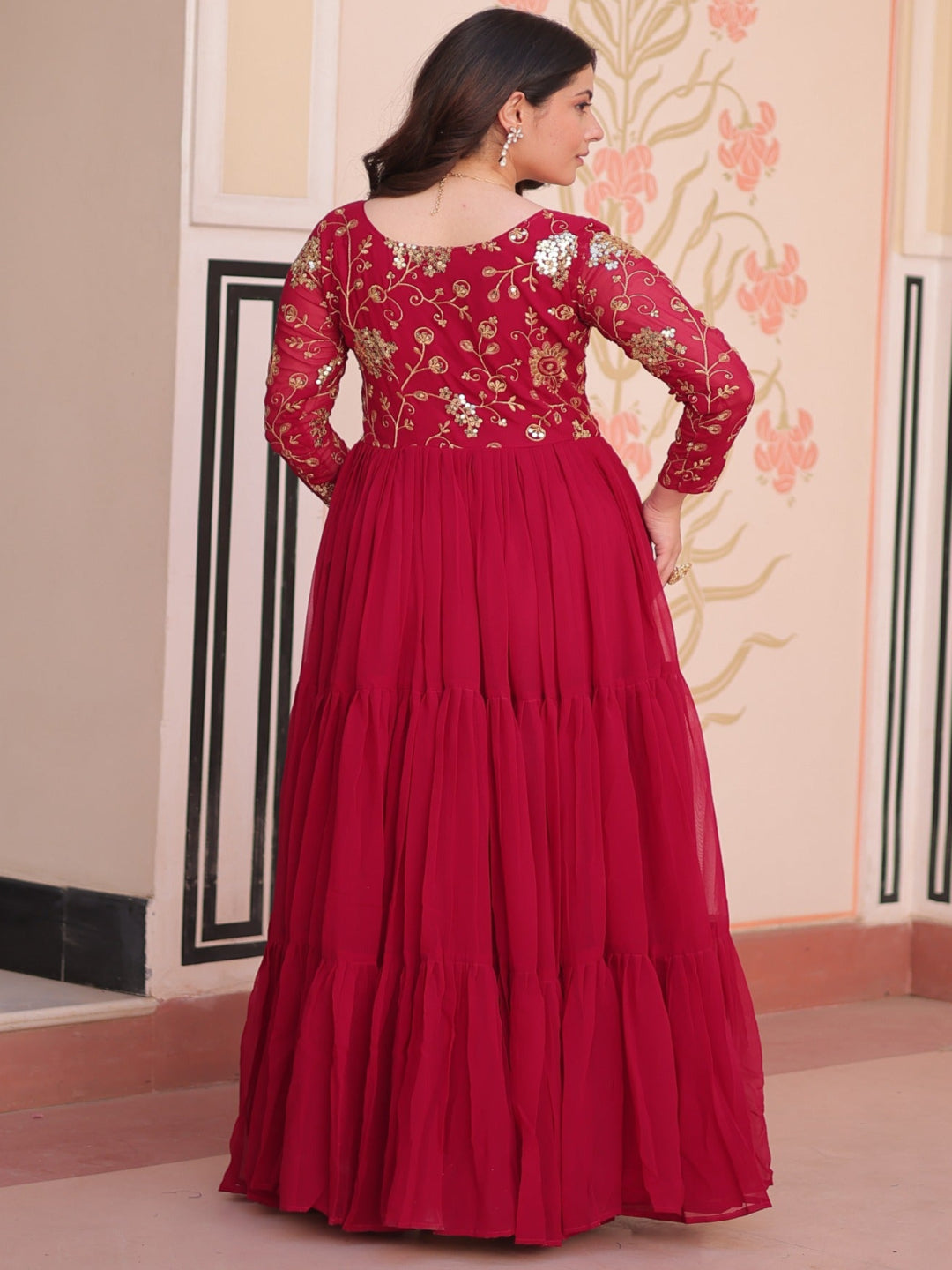 Woman wearing a red traditional outfit with floral patterns in a decorated room.