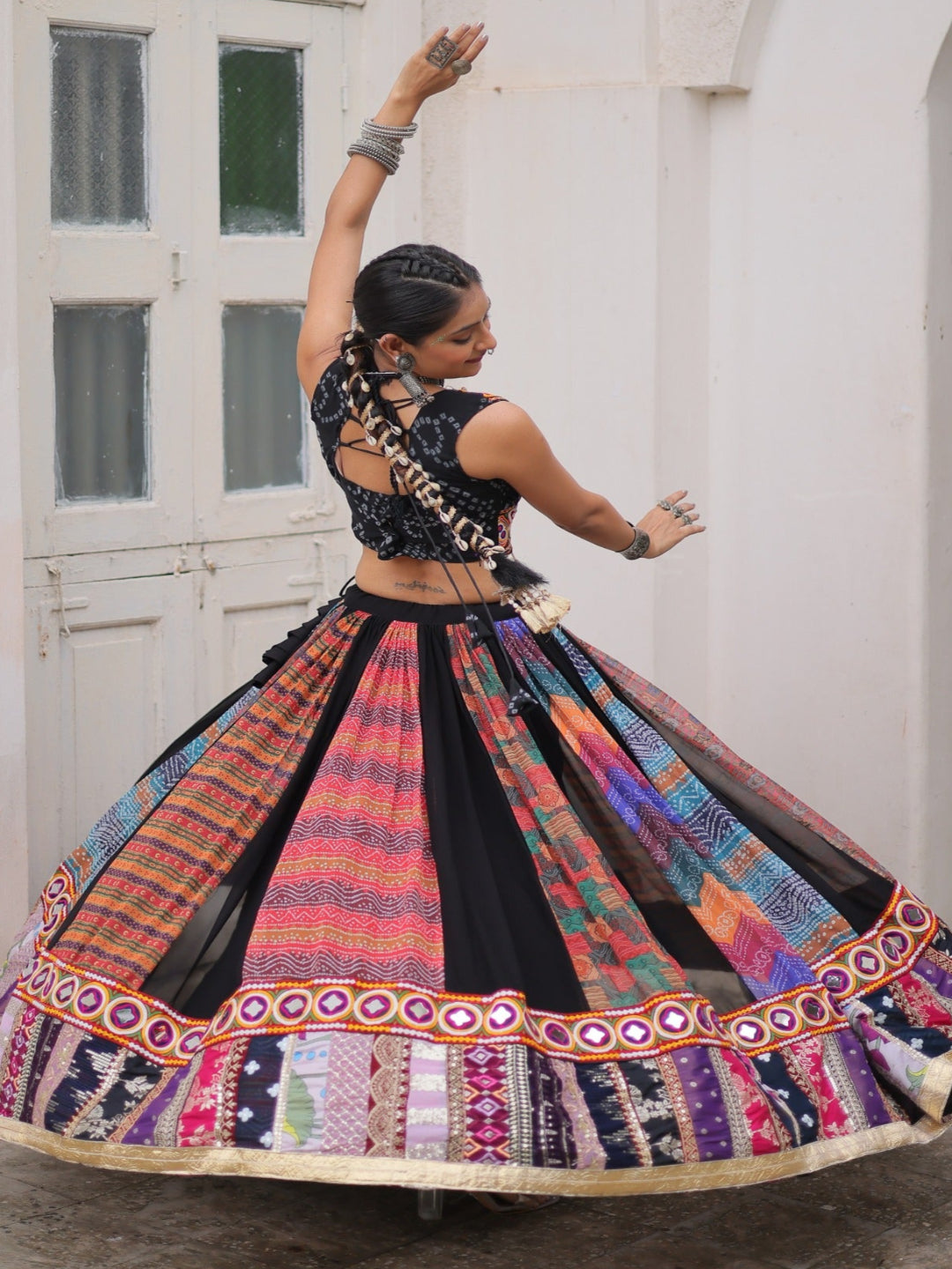 Woman in a colorful traditional outfit dancing in front of a white building with arched doorways.