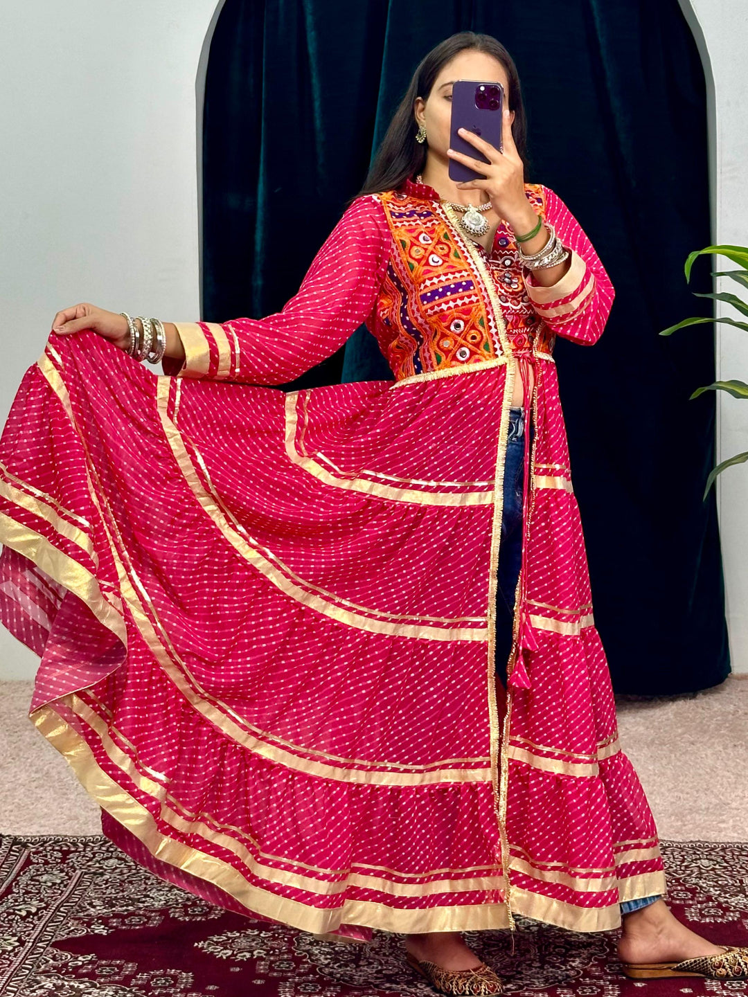 Person wearing a traditional outfit with a pink saree and orange blouse, standing in front of a mirror.