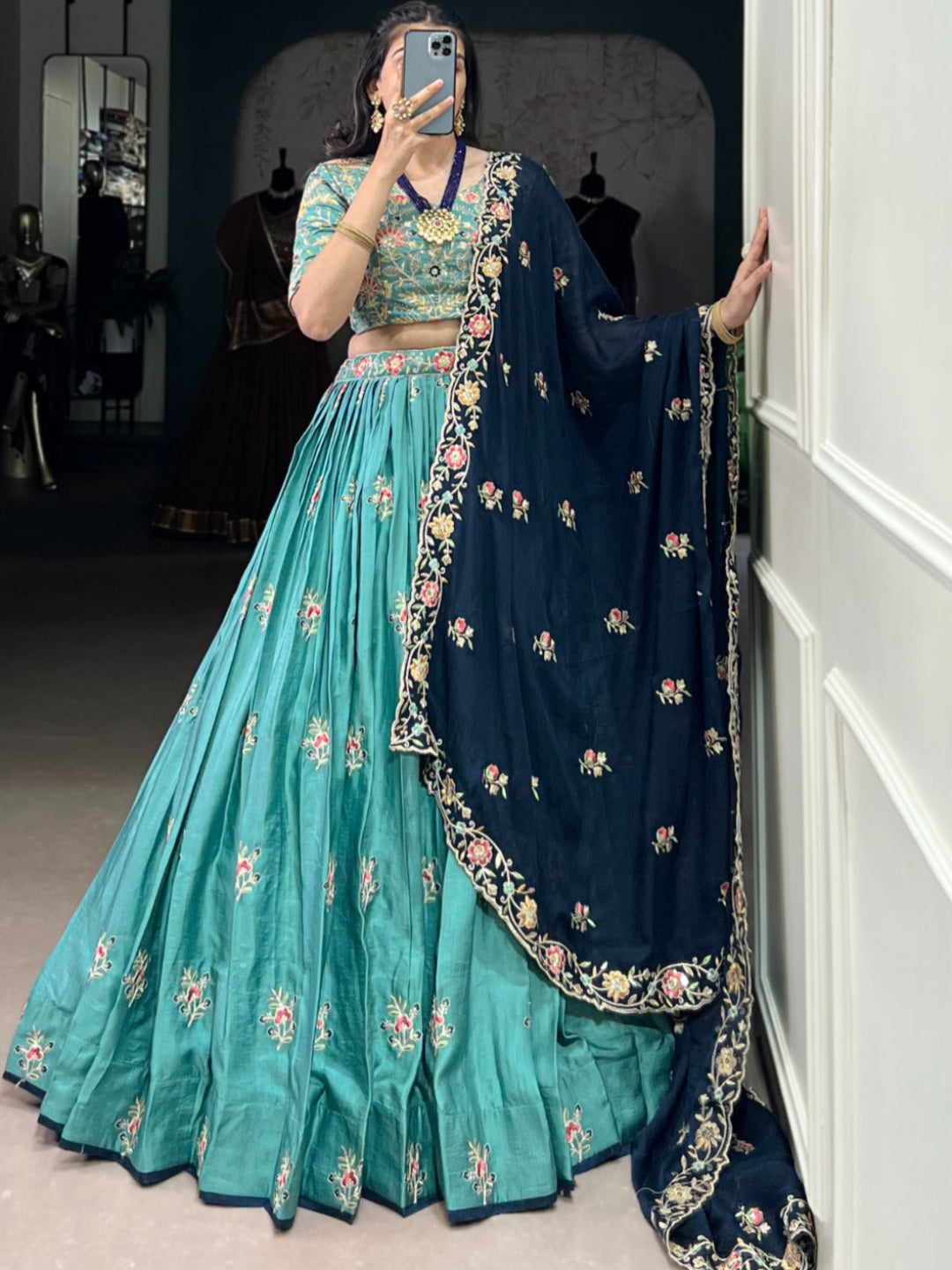 Person wearing a traditional outfit with a teal lehenga and navy dupatta in a room.