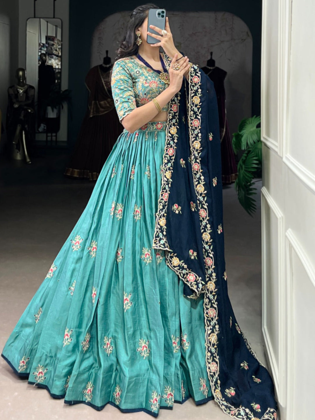 Woman taking a mirror selfie wearing a teal and navy traditional outfit with floral patterns.
