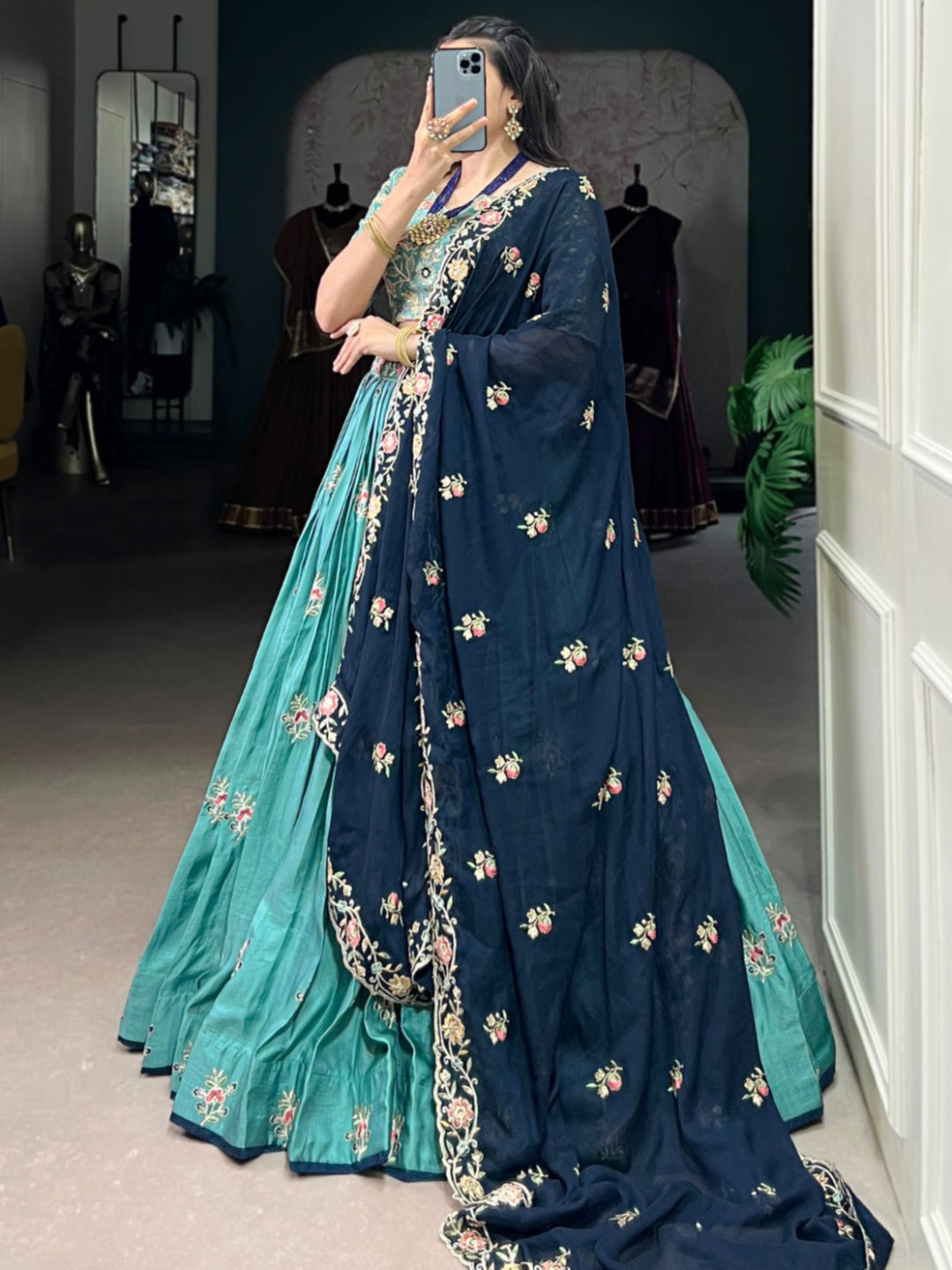 Person wearing a blue and green traditional outfit with floral patterns in a room.