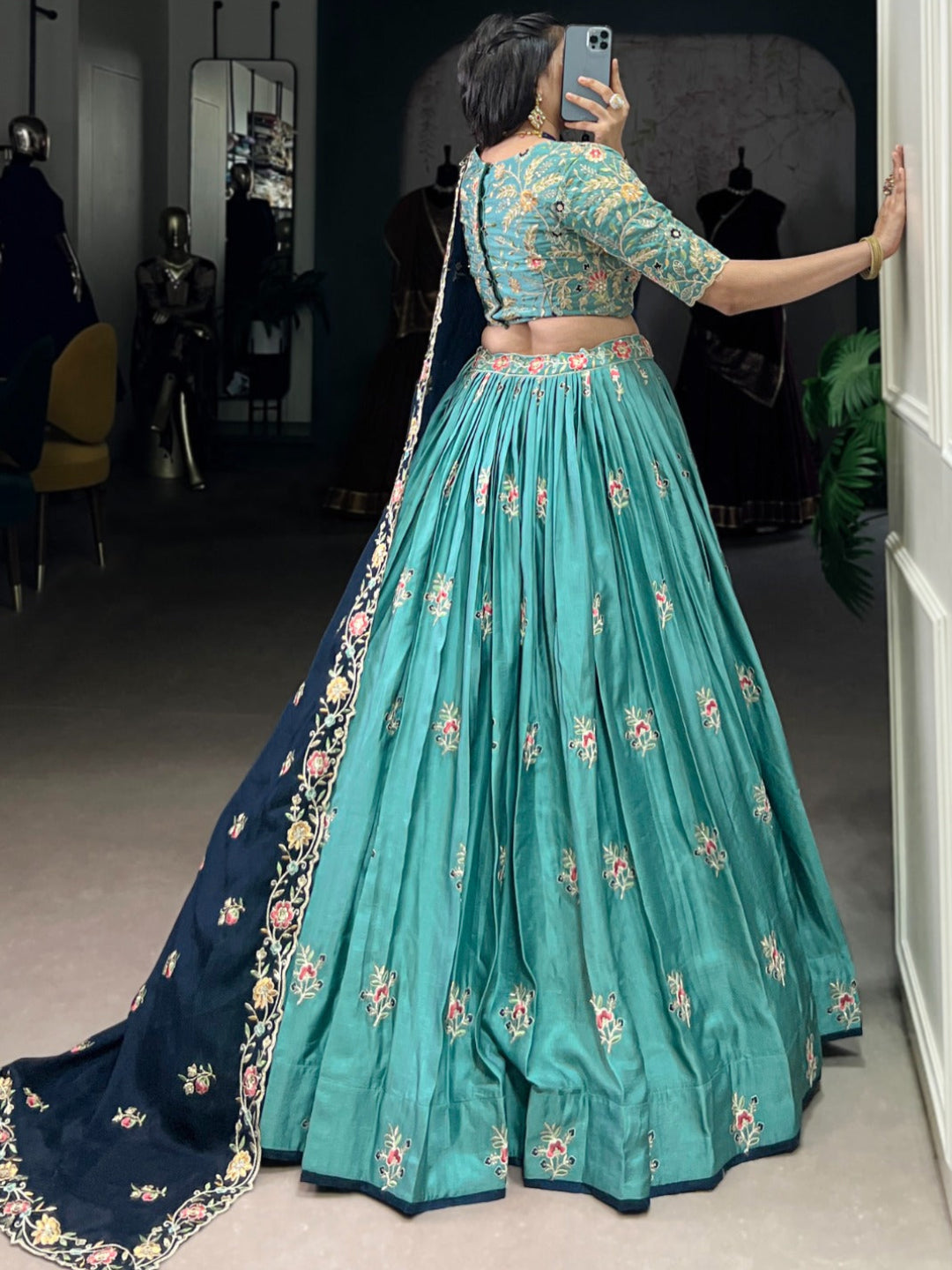 Person wearing a teal and navy embroidered traditional outfit taking a mirror selfie.