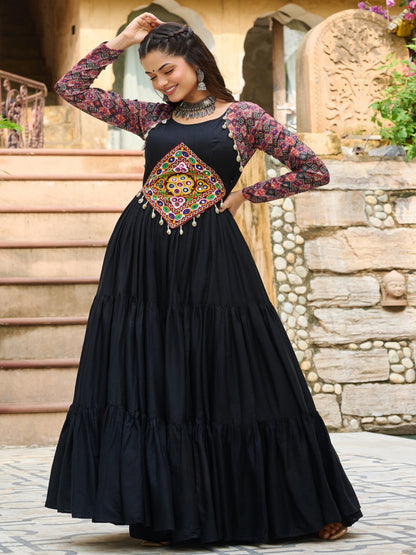 Woman in a black dress with floral sleeves and a colorful belt standing outdoors.