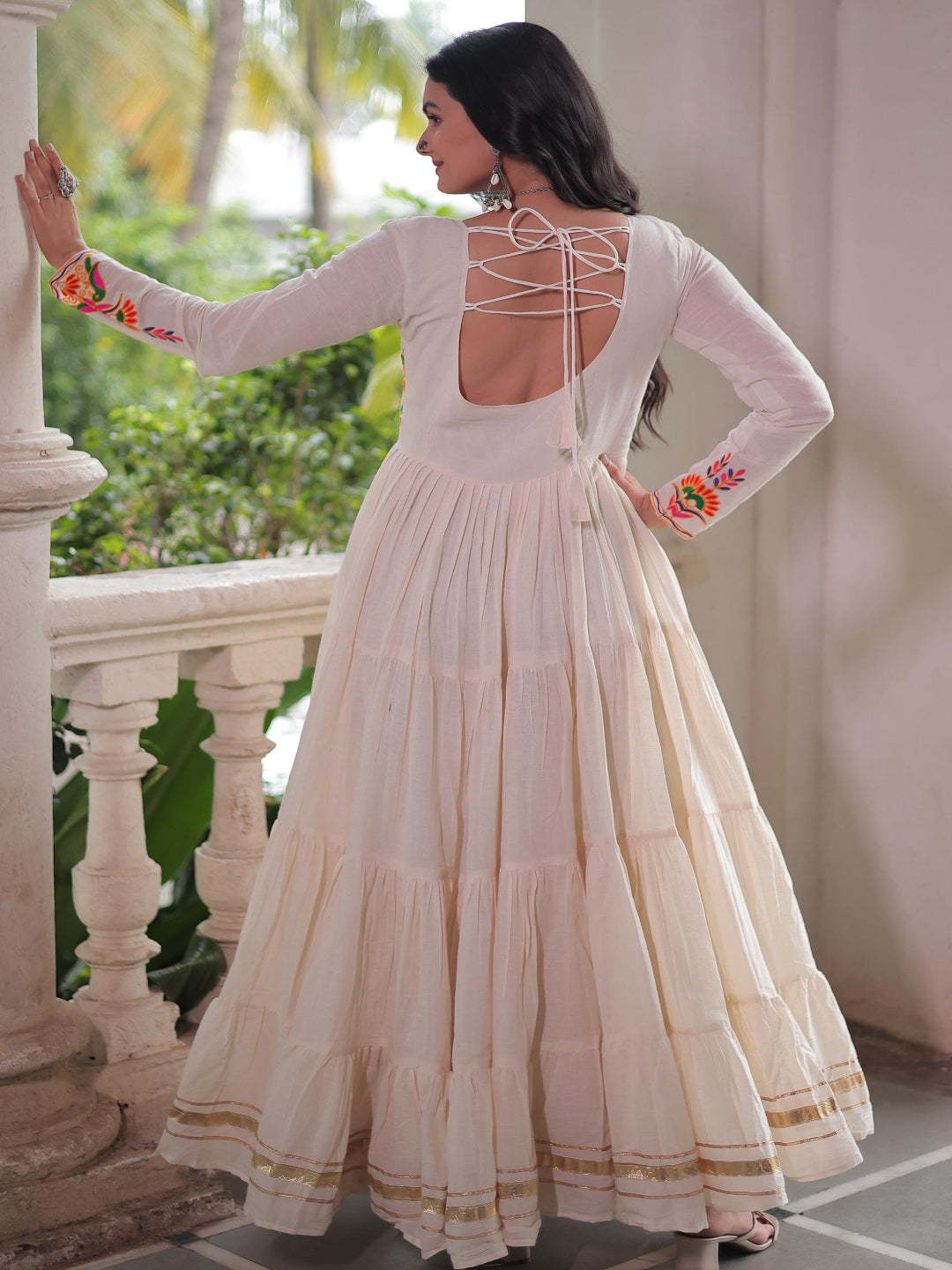Woman in a white traditional outfit with floral sleeves standing on a balcony.